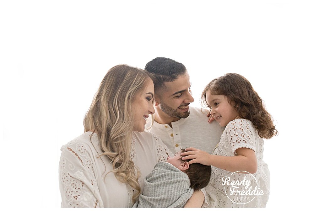 Family of 4 during newborn portrait session in all white photography studio | Ready Freddie Studios in Miami, FL