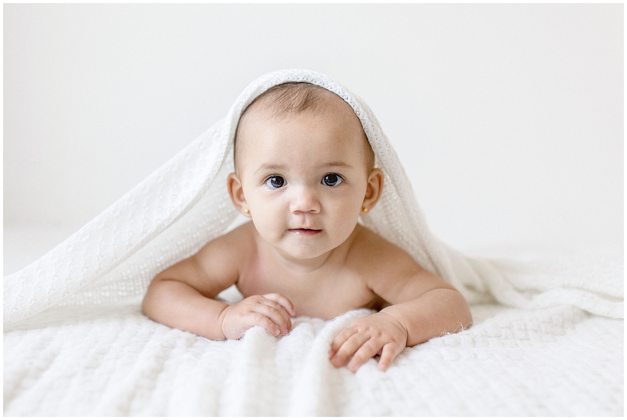 Baby girl plays peek a boo under blanket. Photos by Ivanna Vidal Photography.