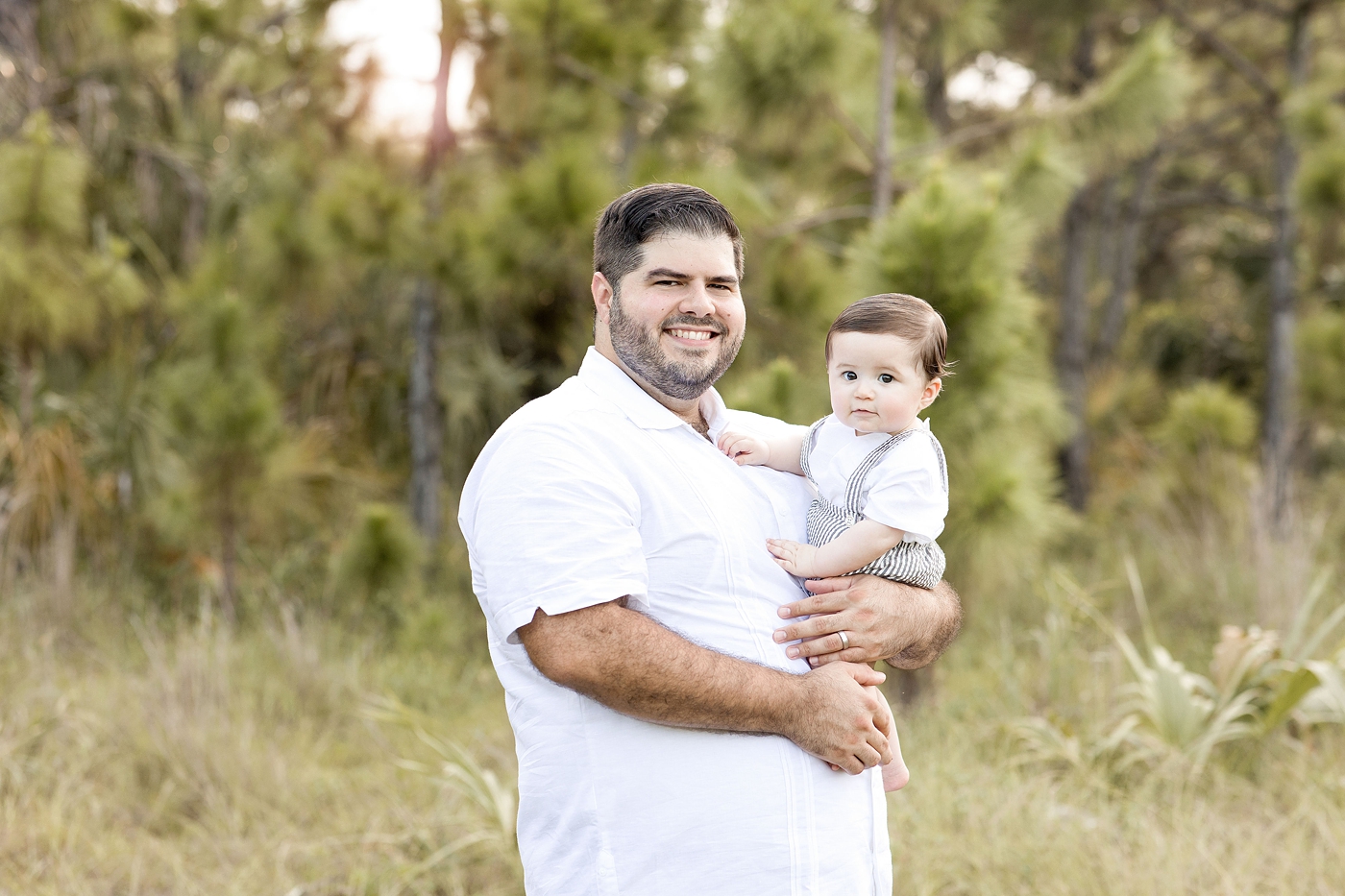 Dad holds young son proudly while smiling at Miami Children Photographer. Photo by Ivanna Vidal Photography.