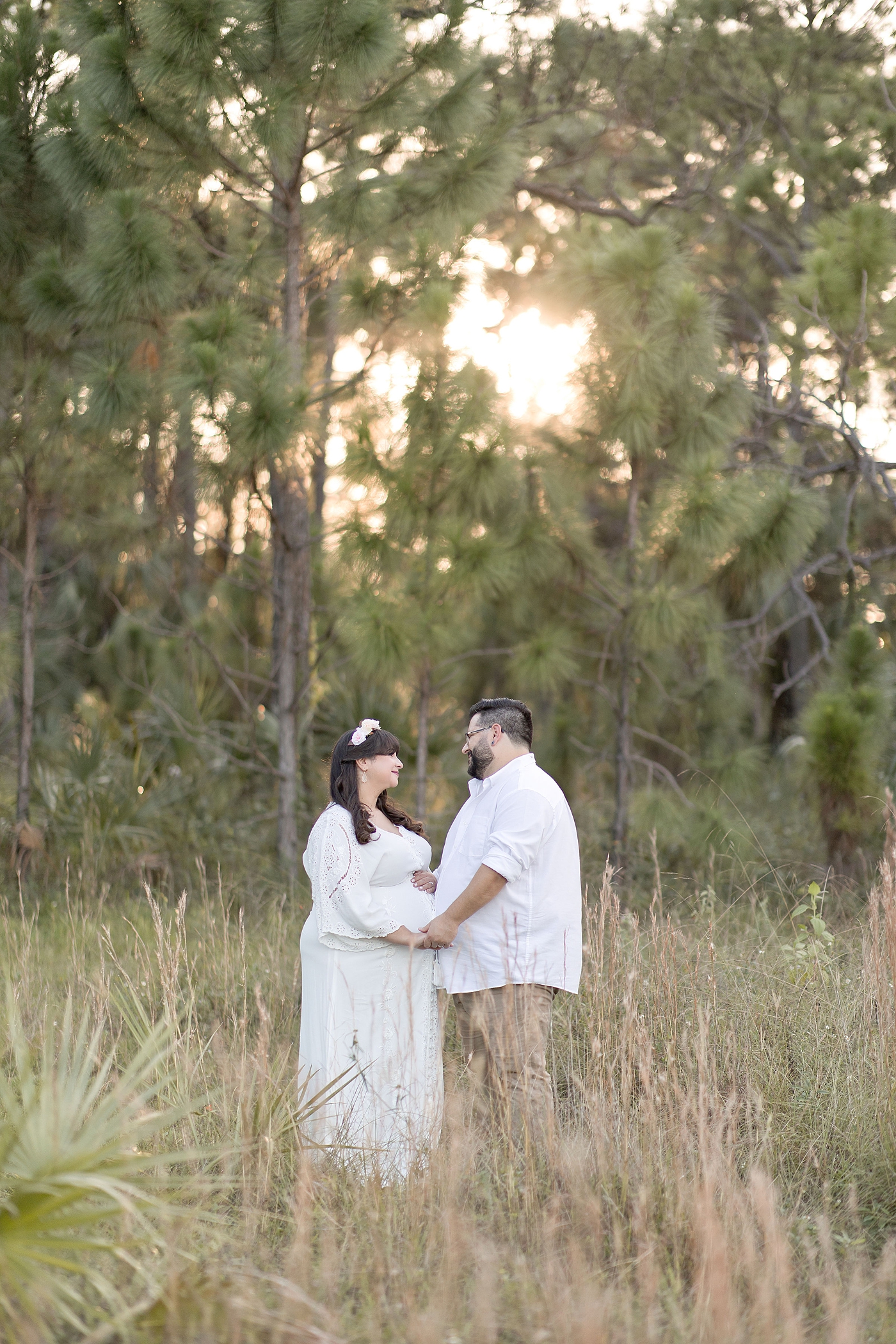Mom and dad to be hold hands in field. Photo by South Florida Maternity Photographer Ivanna Vidal Photography.
