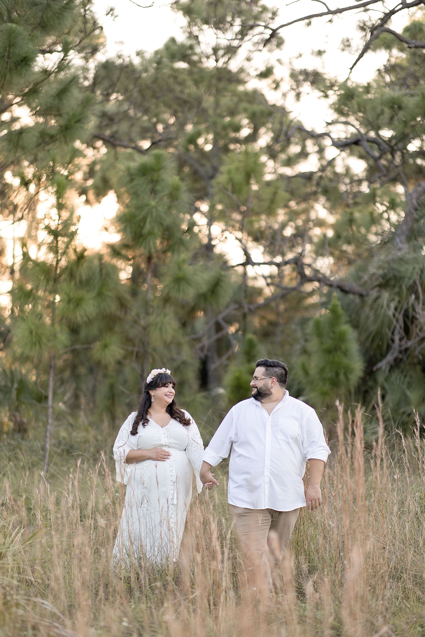 Plus Size Maternity Photoshoot with Mom and dad walk in field during Miami maternity session. Photo by South Florida Maternity Photographer Ivanna Vidal Photography.