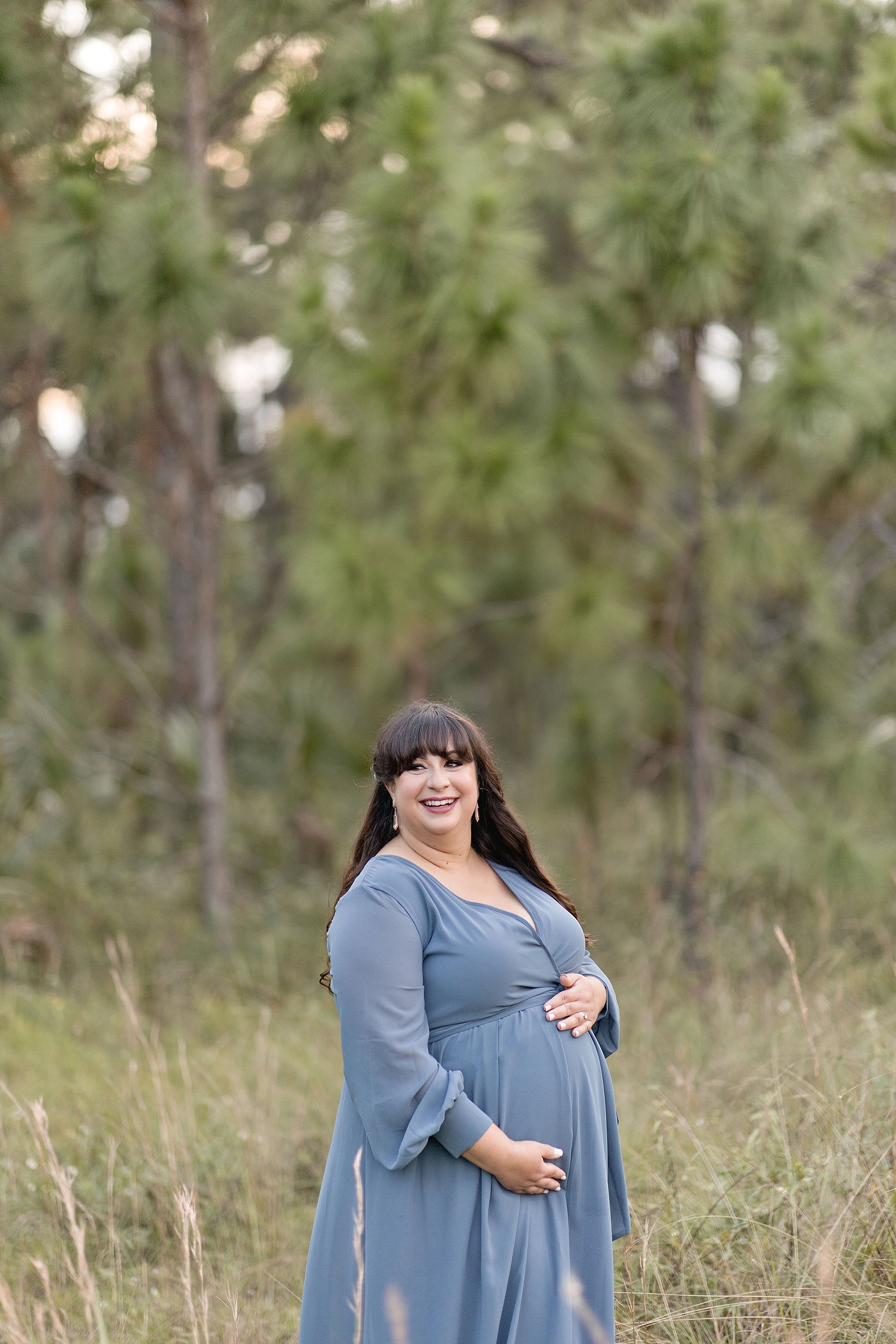 Plus Size Maternity Photoshoot with Mom smiles in blue dress during mother nature inspired maternity session. Photo by South Florida Maternity Photographer Ivanna Vidal Photography.