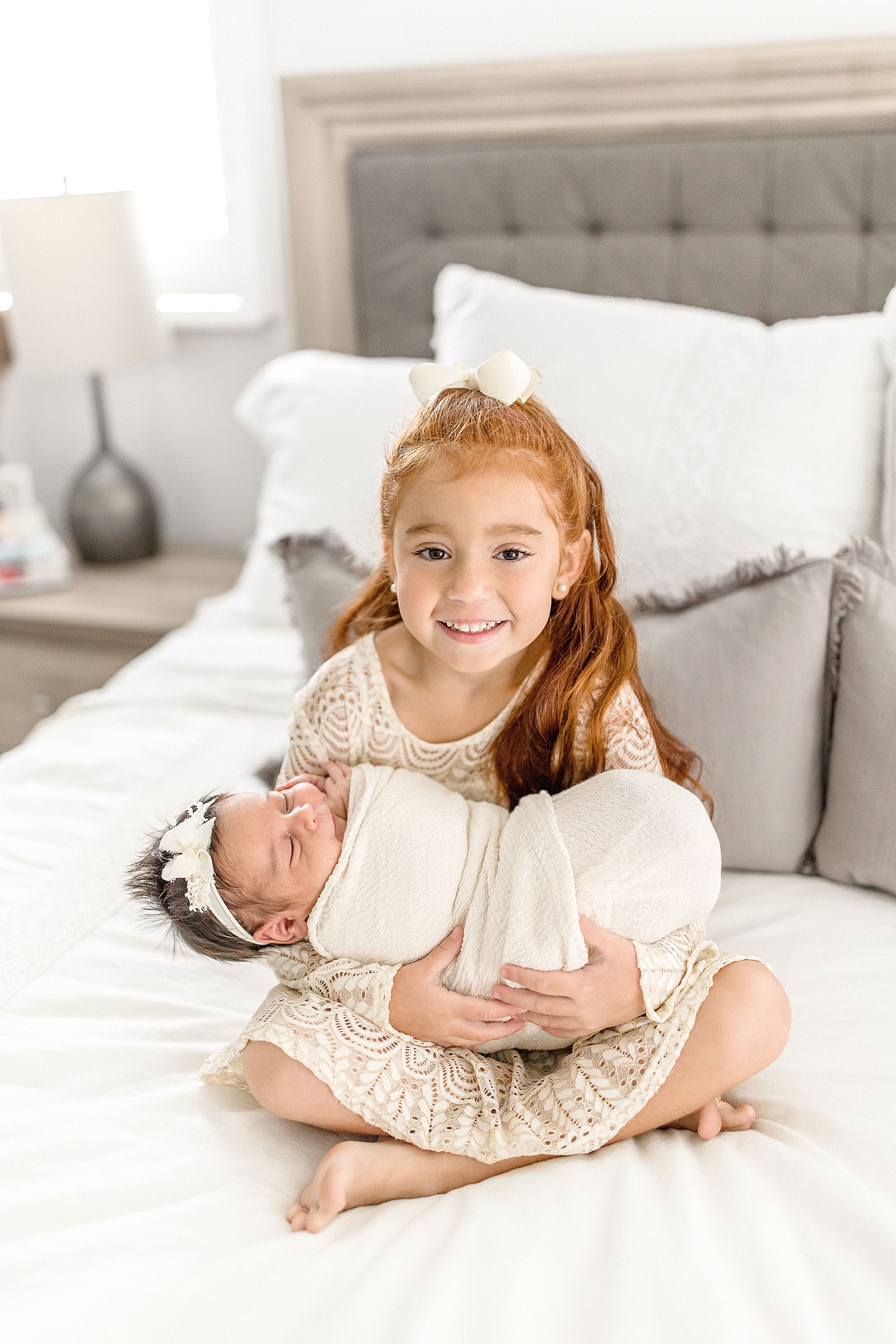 Older sister proudly holds brand new baby sister during in home Miami Lifestyle newborn session. Photo by Ivanna Vidal Photography.