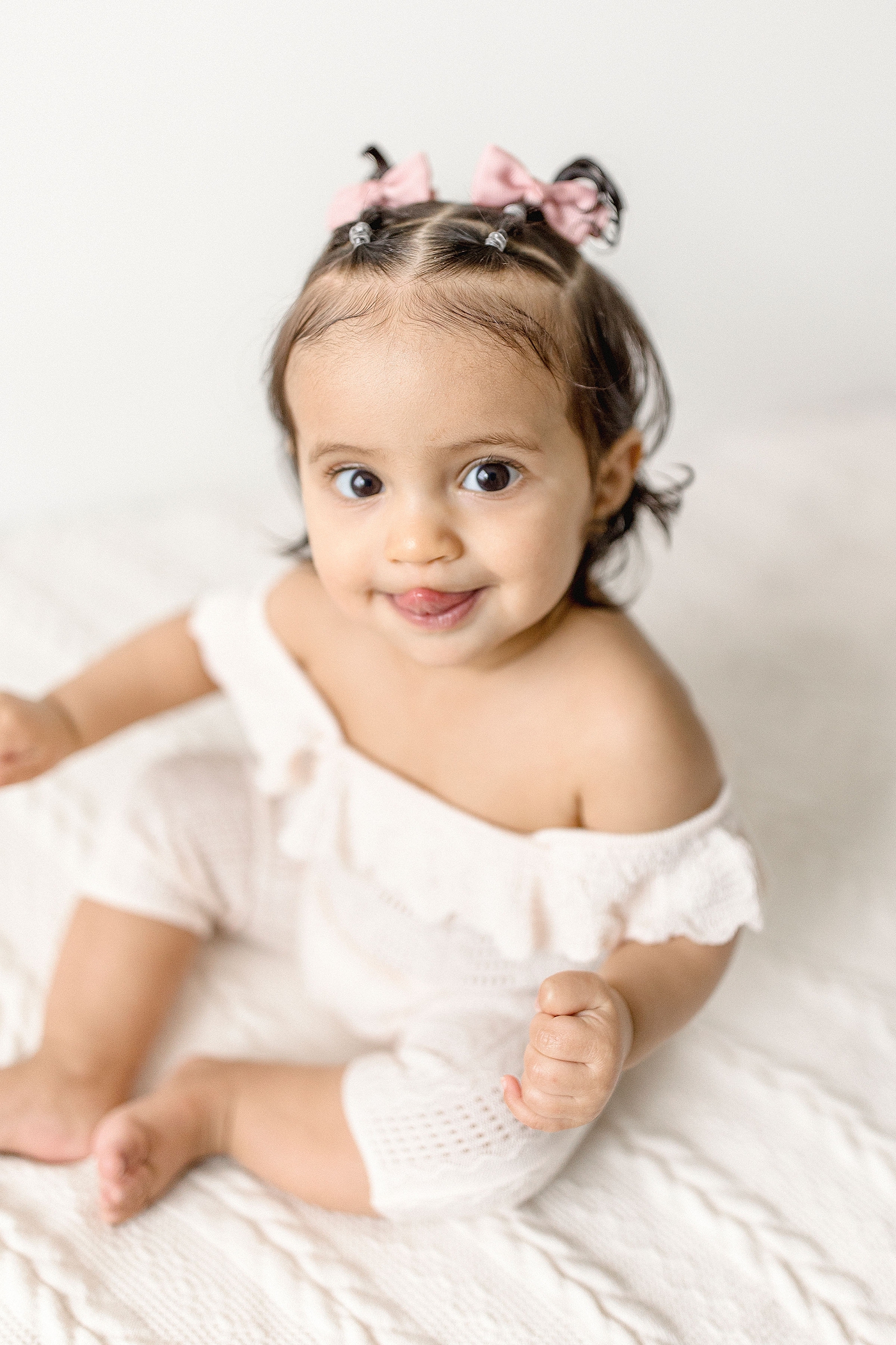 Six month sitter session of baby girl in pigtails and white romper during her baby photography miami session. Photo by Ivanna Vidal Photography.