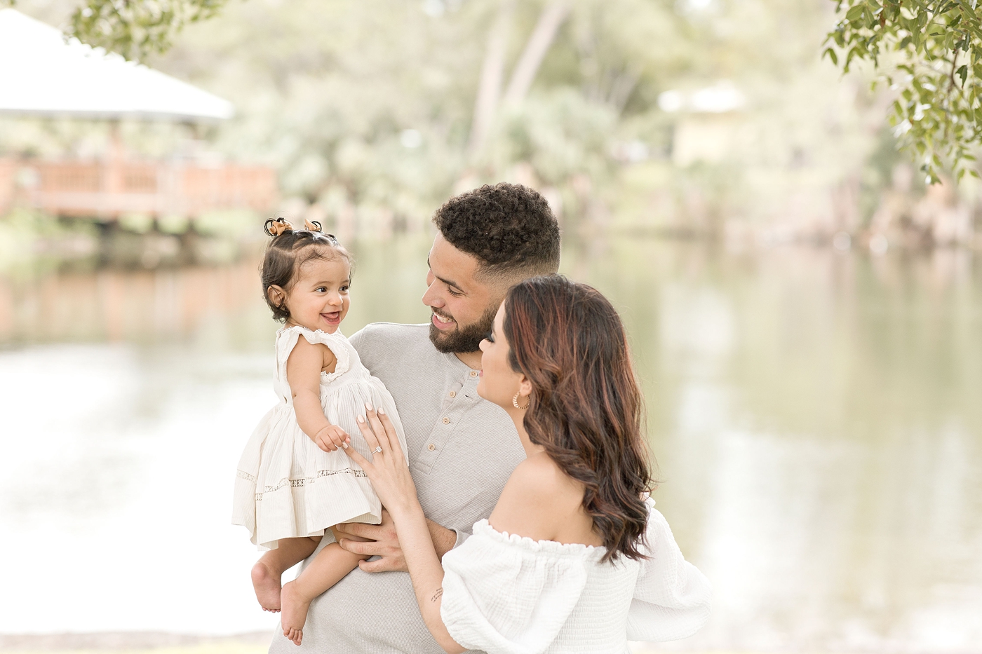 Little girl smiles as mom and dad make her laugh during baby photography miami session. Photo by Ivanna Vidal Photography.