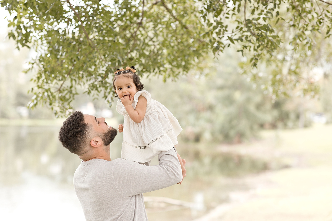 Dad holds up baby girl by the water during baby photography miami session. Photo by Ivanna Vidal Photography.