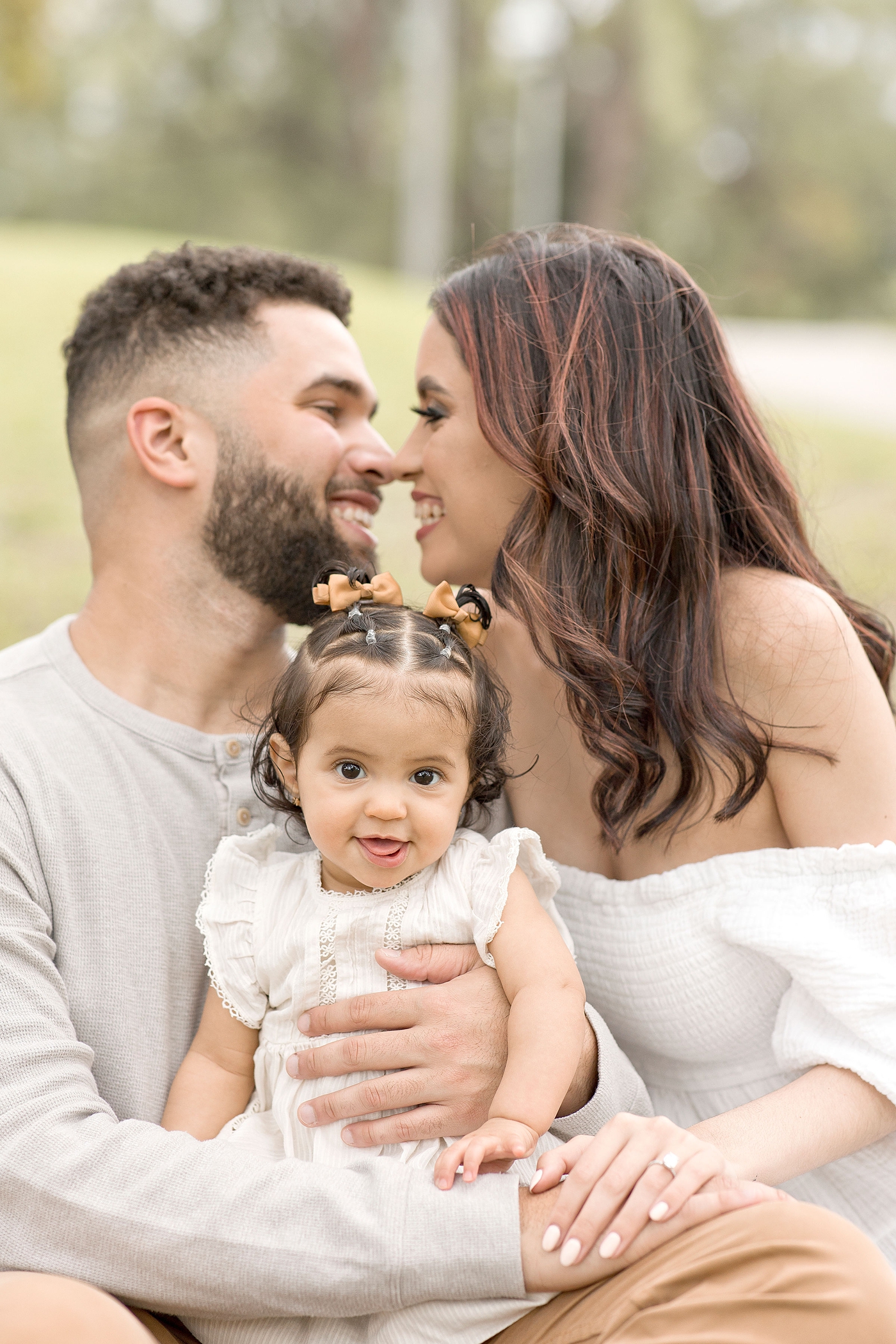 Dad and mom connect noses while baby grins for camera during baby photography miami session. Photo by Ivanna Vidal Photography.