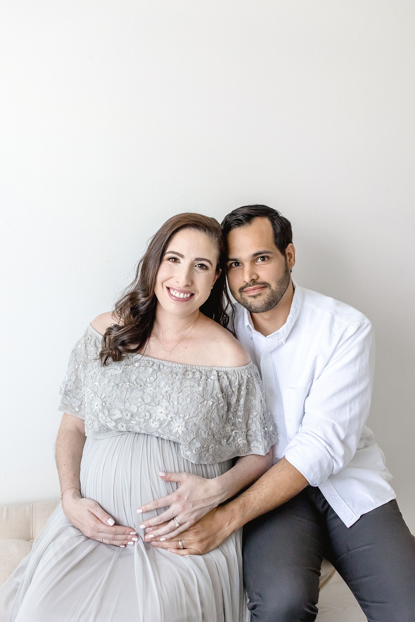 Expecting couple smile for photographing during maternity studio session before going to El Farito Beach Miami FL. Photo by Ivanna Vidal Photography.