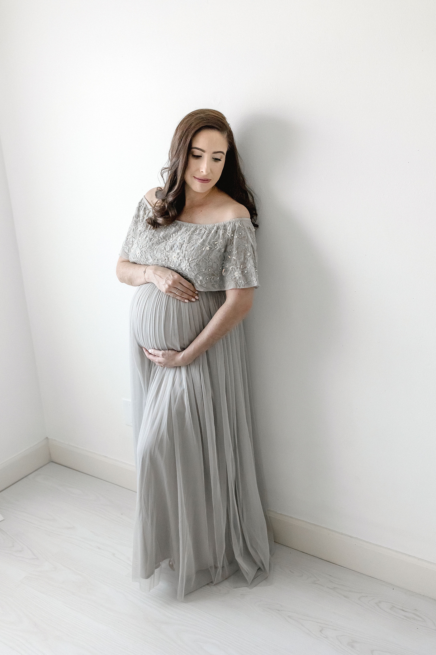 Mom to be holds her bump while leaning against wall during maternity session before headed to El Farito Beach Miami FL. Photo by Ivanna Vidal Photography.