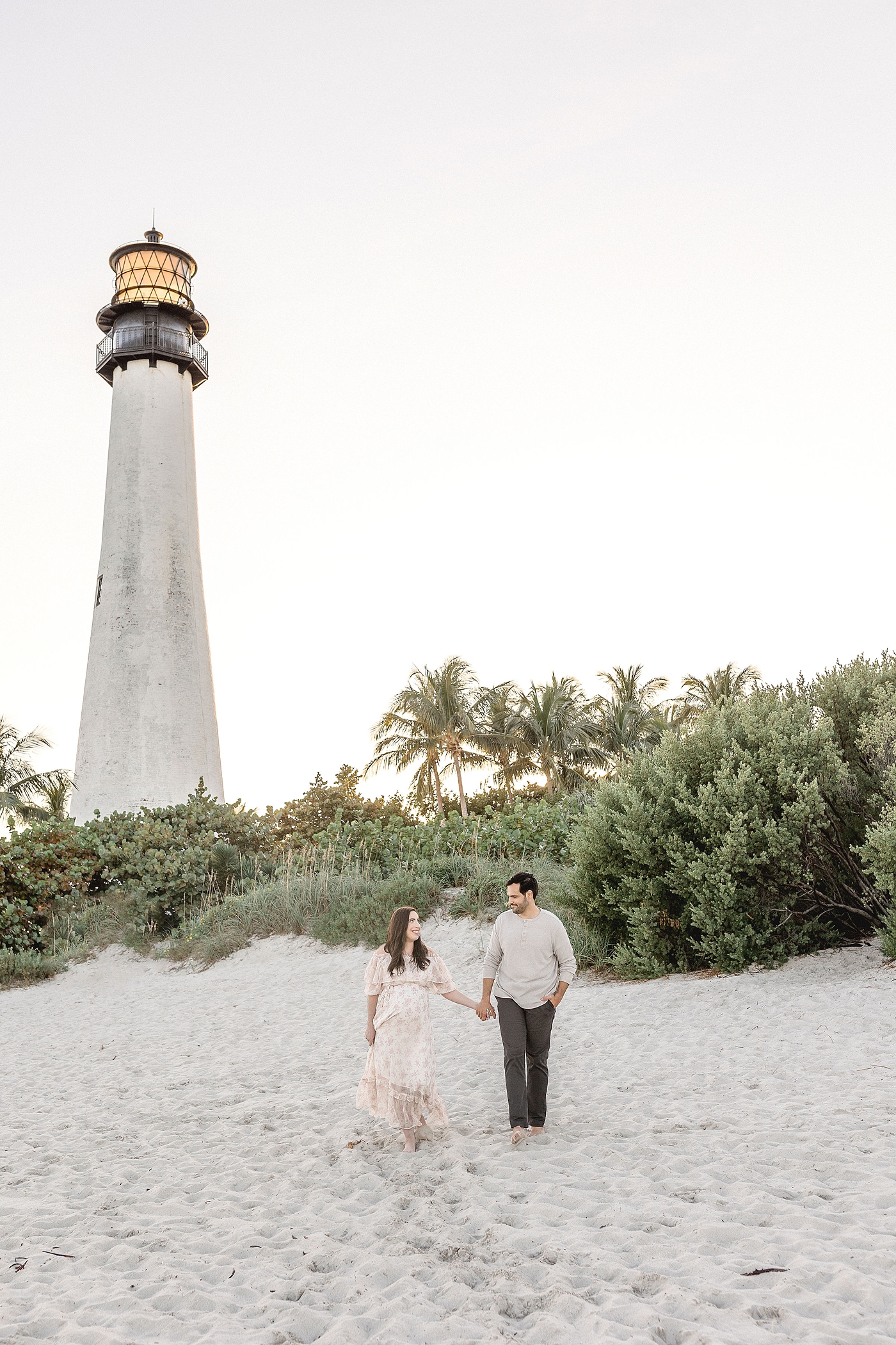 Expectant parents walk in front of El Farito Beach Miami FLduring their maternity session. Photo by Ivanna Vidal Photography.