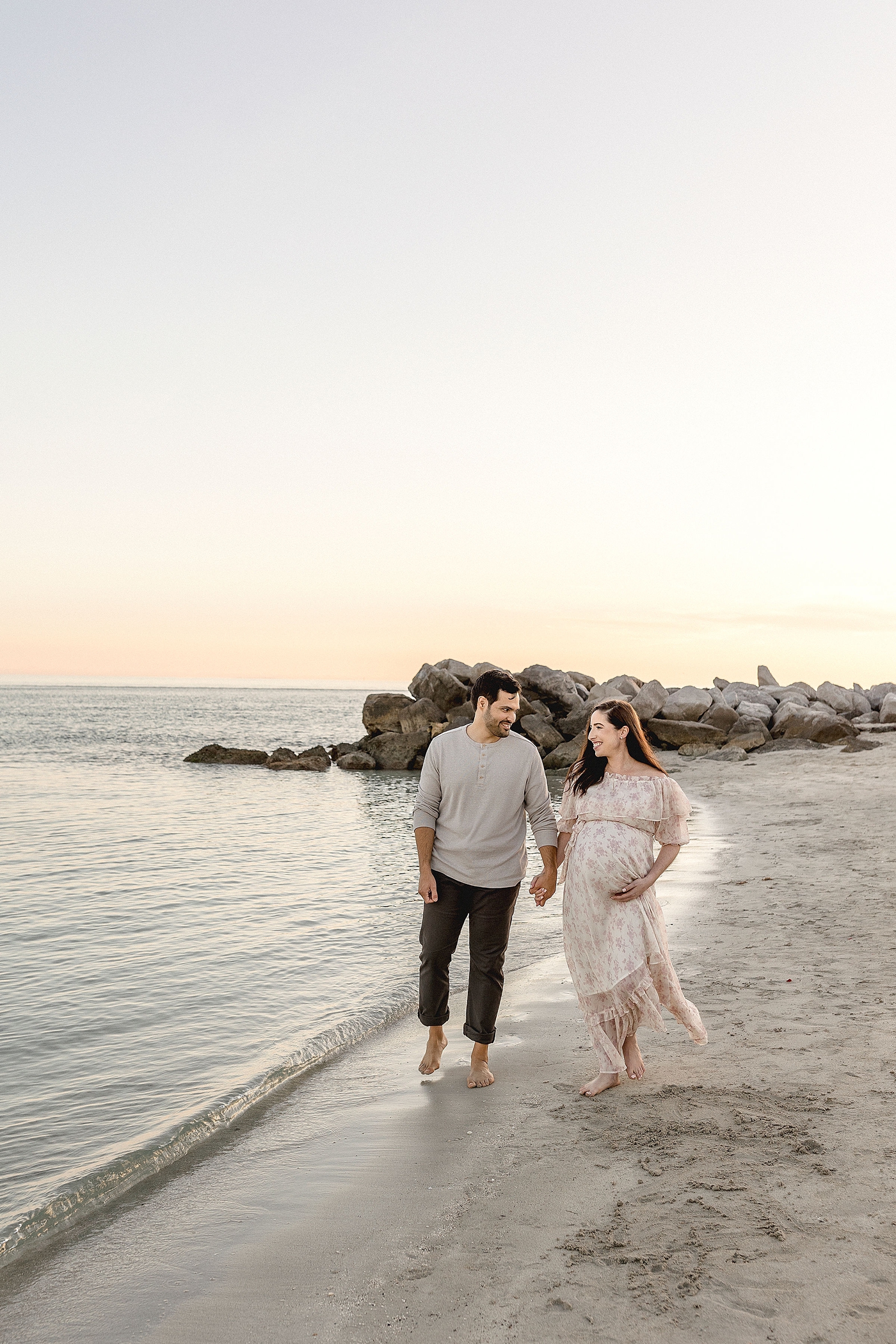 Mom and Dad share in excitement for their new baby while walking along the water's edge at El Farito Beach Miami FL. Photo by Ivanna Vidal Photography.