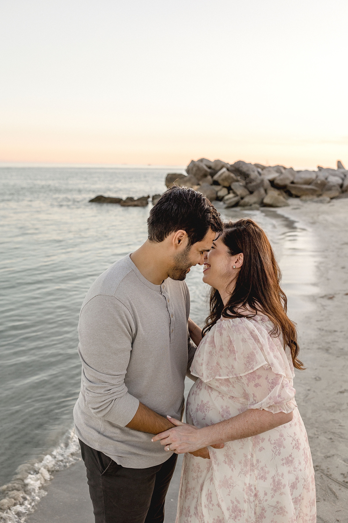 Expecting parents embrace at the shore's edge at El Farito Beach Miami FL. Photo by Ivanna Vidal Photography.