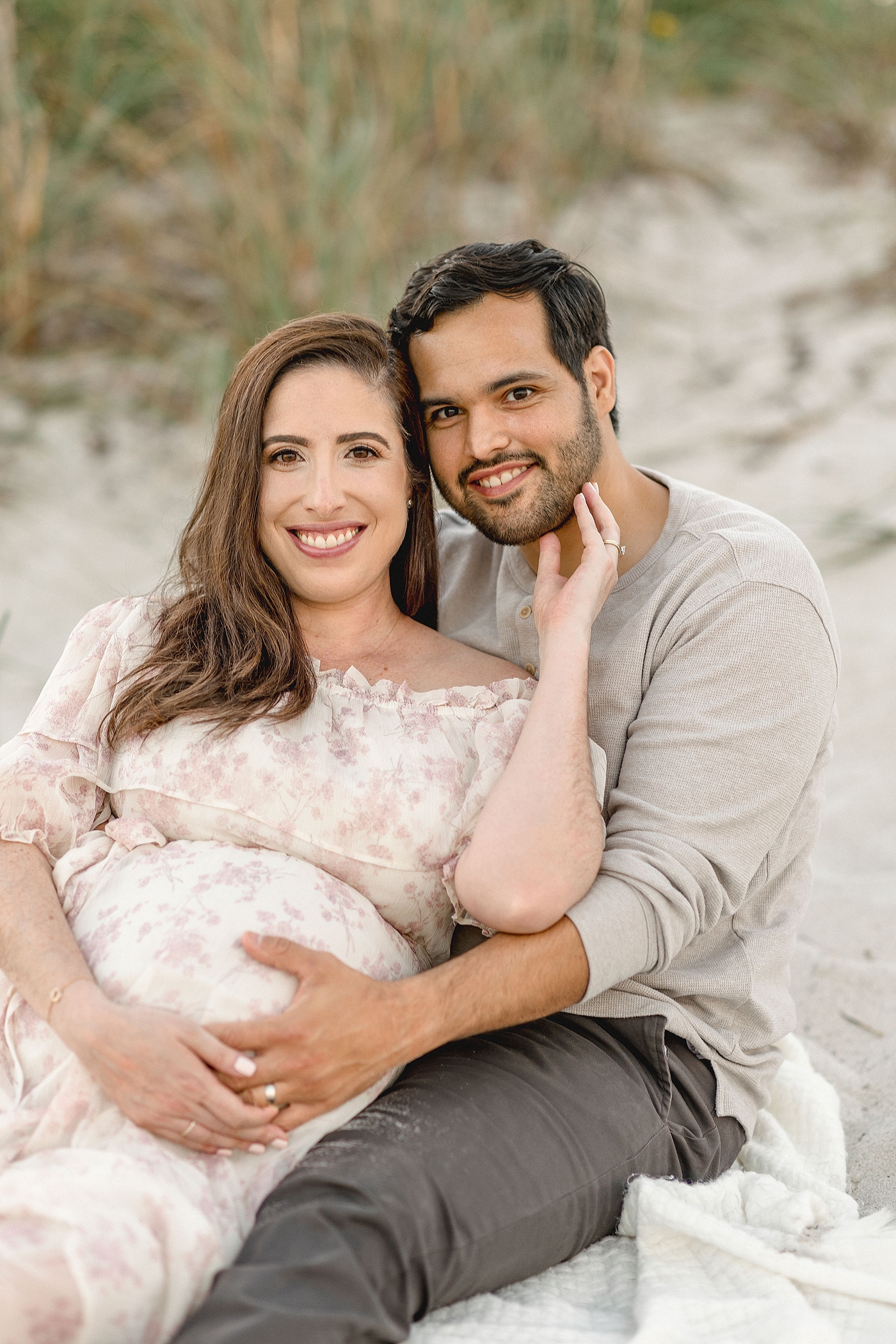 Mom and Dad snuggle while on the beach during their Maternity photos at El Farito Beach Miami FL. Photo by Ivanna Vidal Photography.