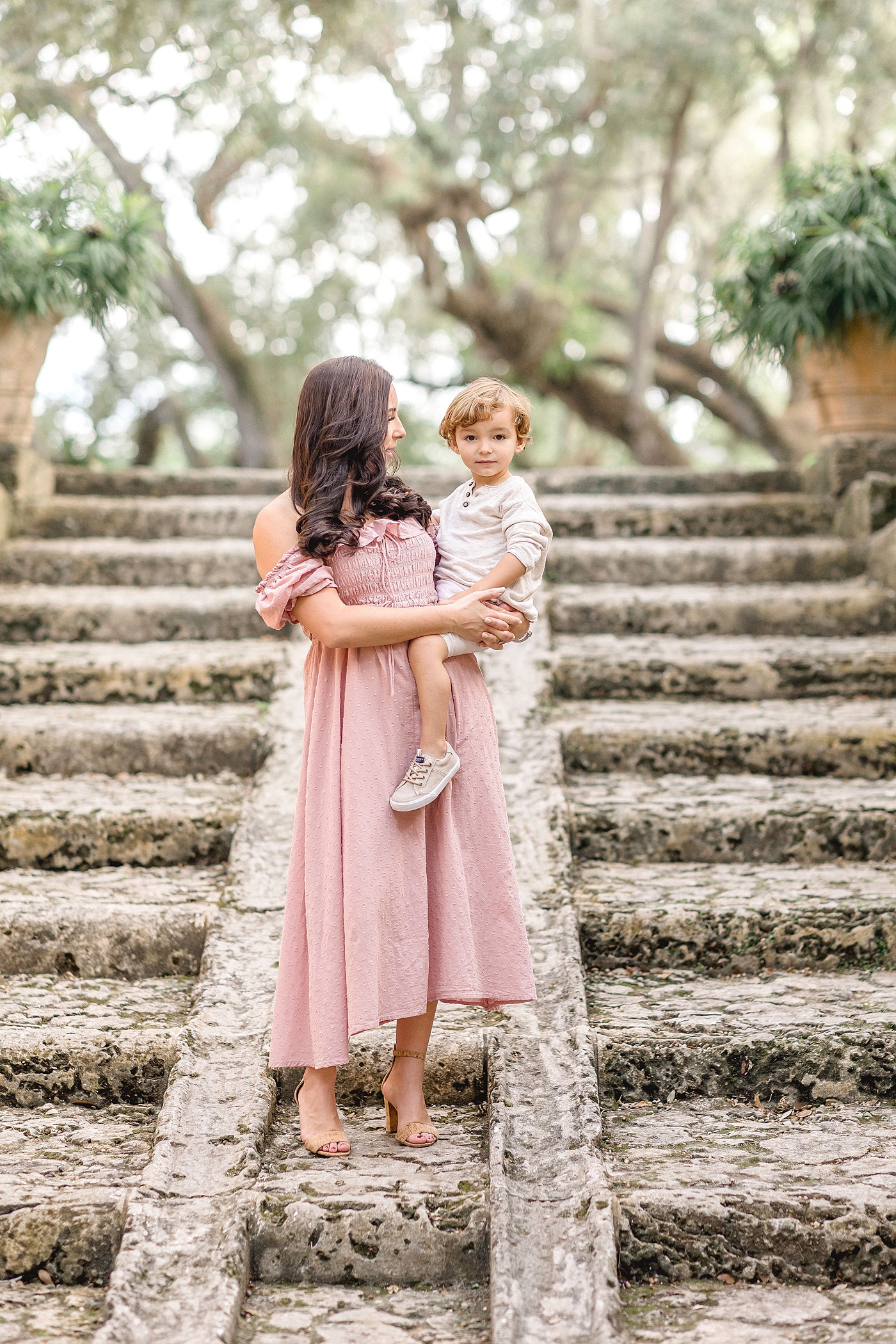 Mom holds son on set of ancient looking stairs during Vizcaya Family photoshoot. Images by Ivanna Vidal Photography.