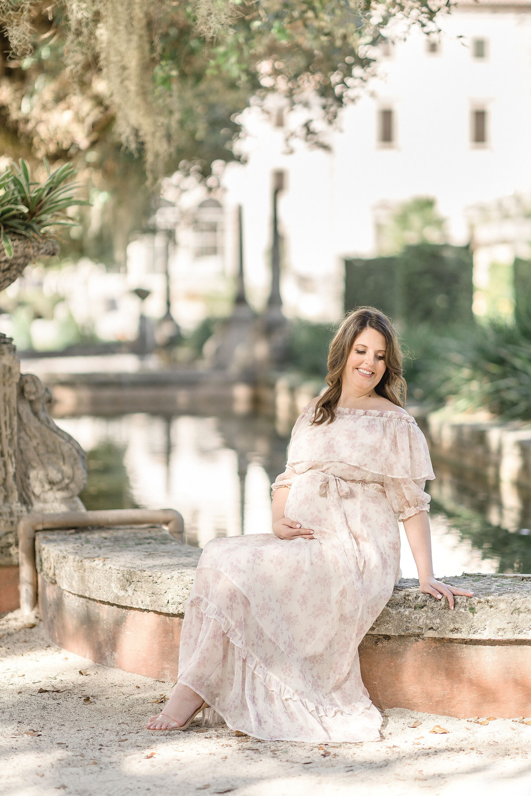 mom to be in floral gown sitting on a stone wall Maternity Clothing Miami