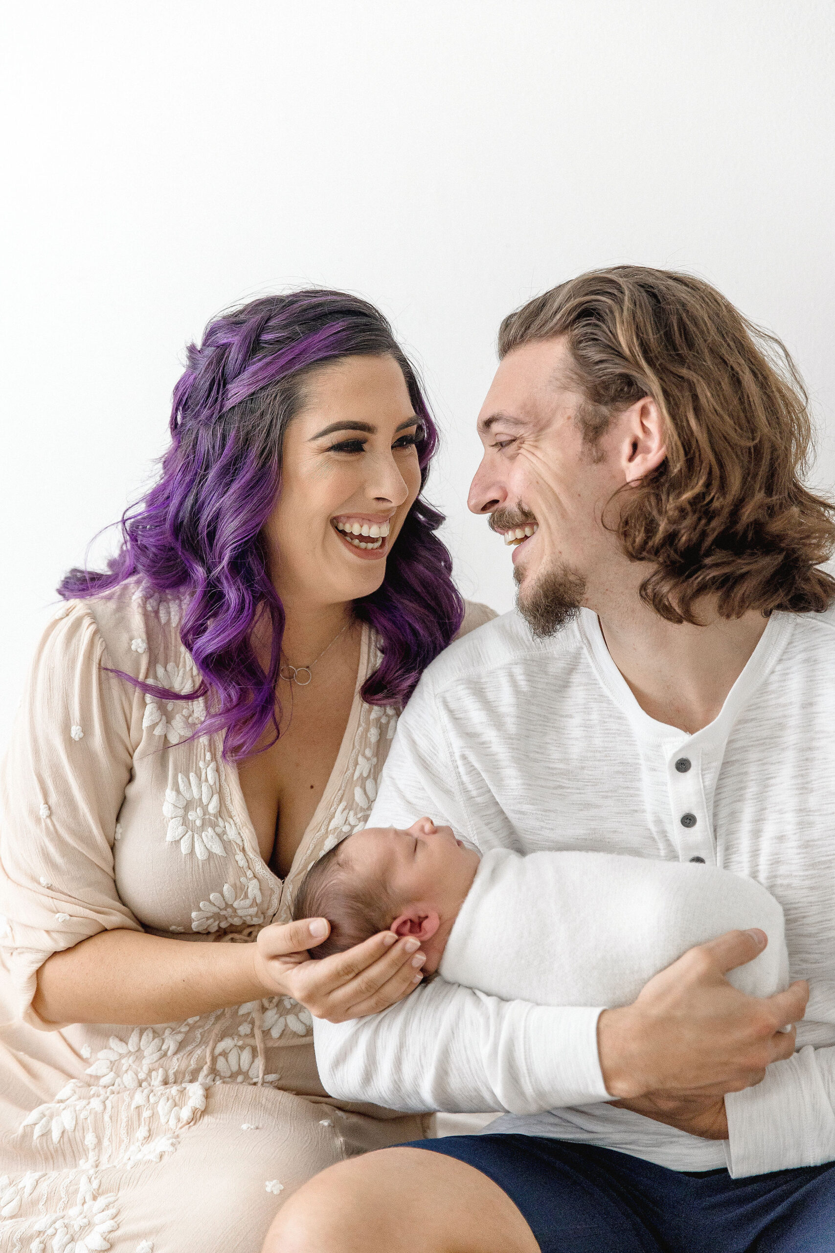 new parents laughing together as they hold their newborn