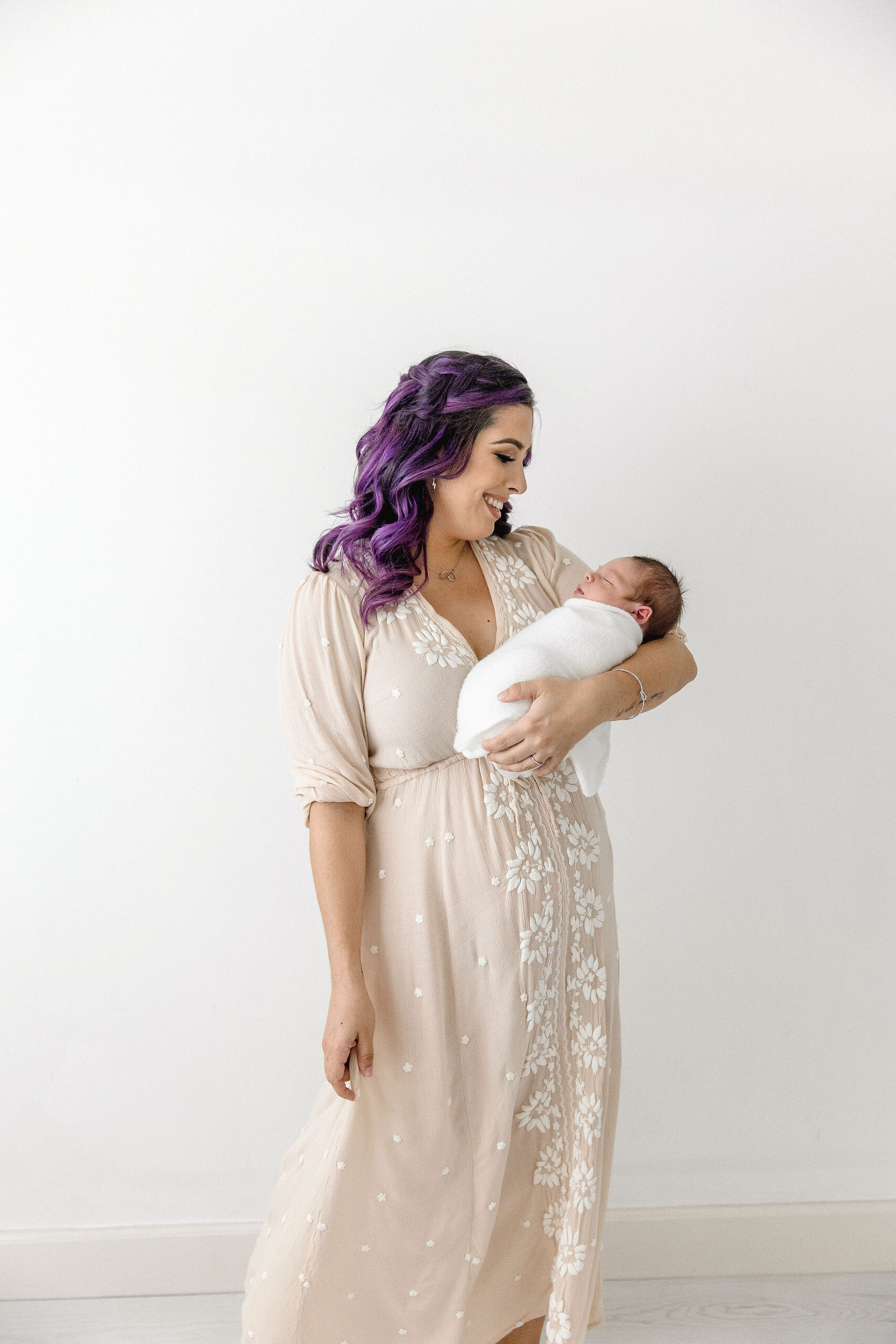 mom in tan dress holding her newborn wrapped in white Miami Lactation Consultant