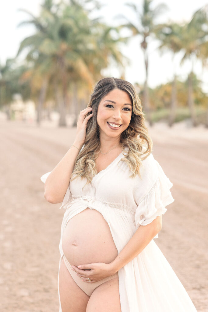 mom to be in white open maternity gown at Crandon Park Maternity Photoshoot locations in Miami