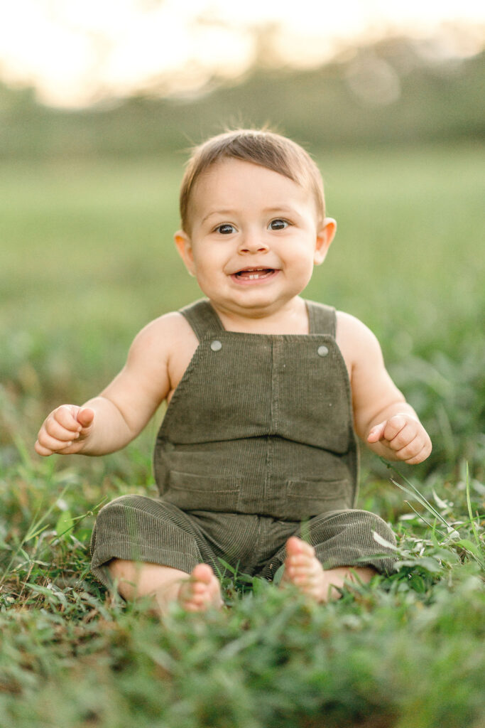 little boy in green overalls sitting in the grass laughing Robbins Lodge