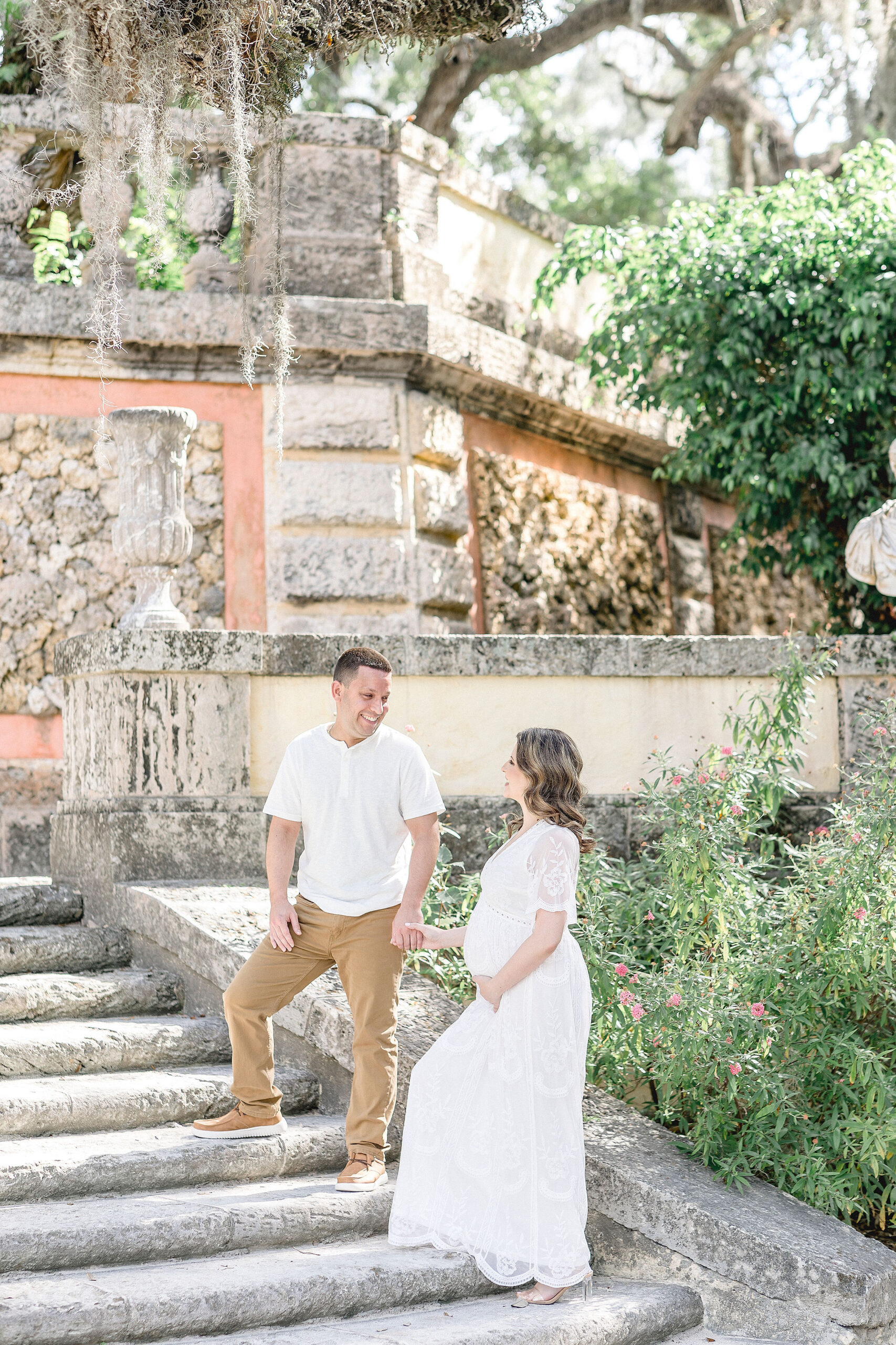 mom and dad to be in white walking up stairs at Vizcaya Museum and Gardens