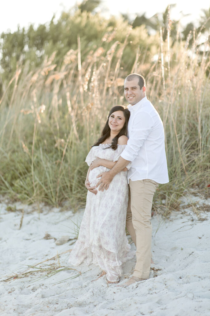 husband cradling his wife's baby bump on the beach Bayshore Women’s Healthcare