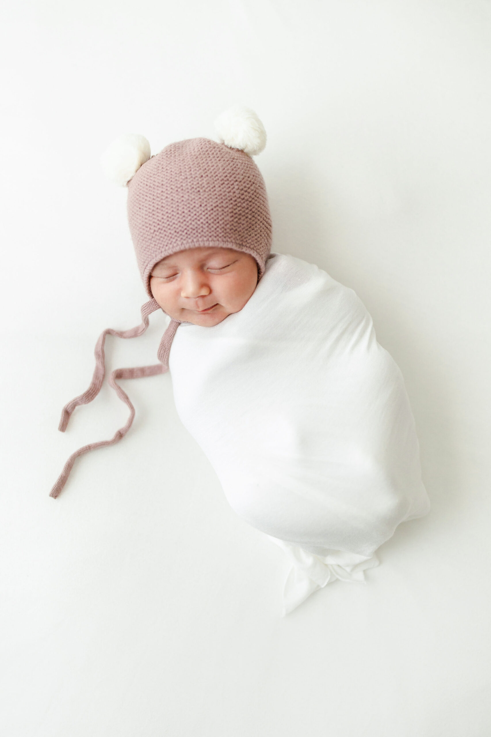 newborn baby wrapped in white with a pink bear hat Caprilina