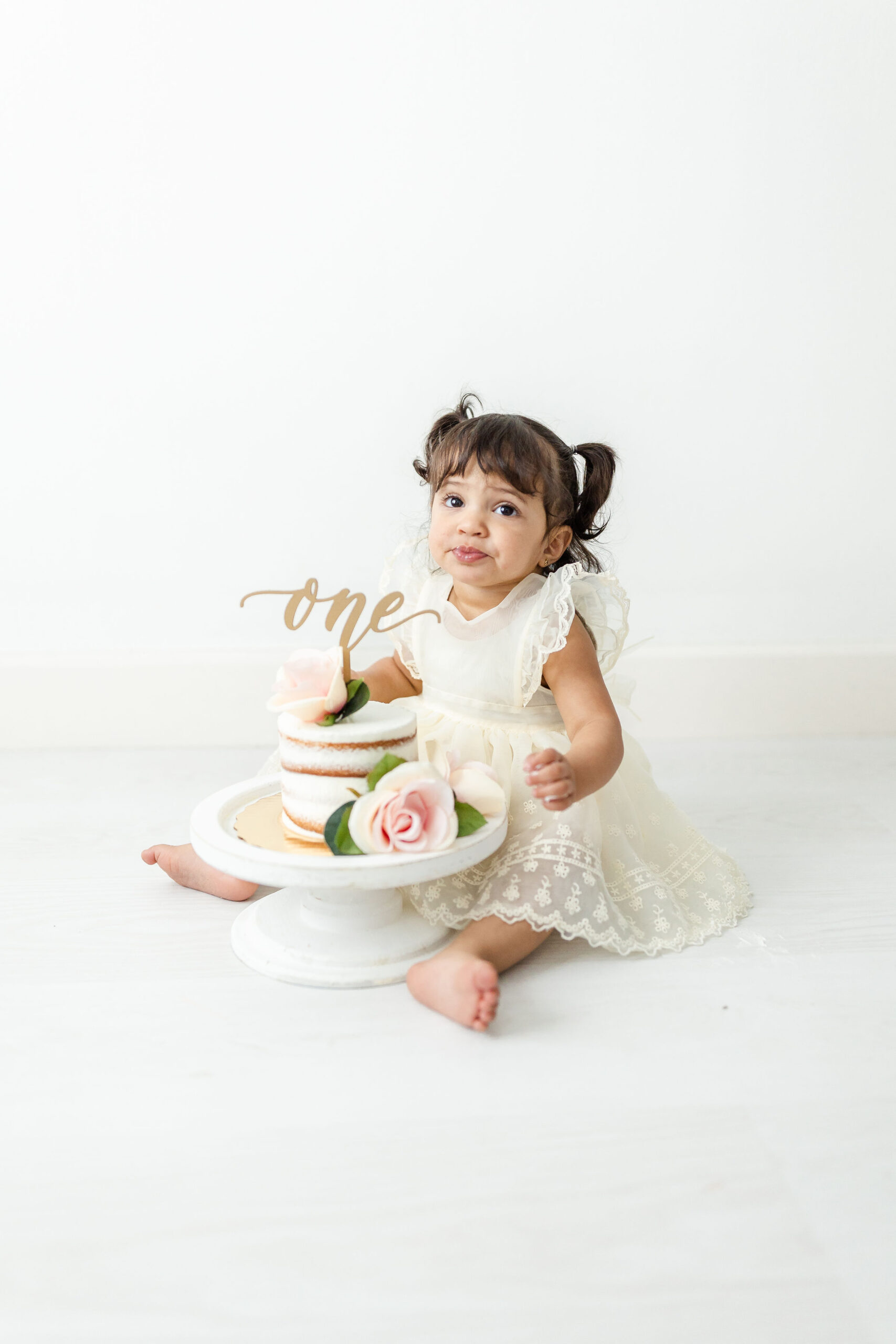 Toddler girl sits in a studio with her first birthday cake