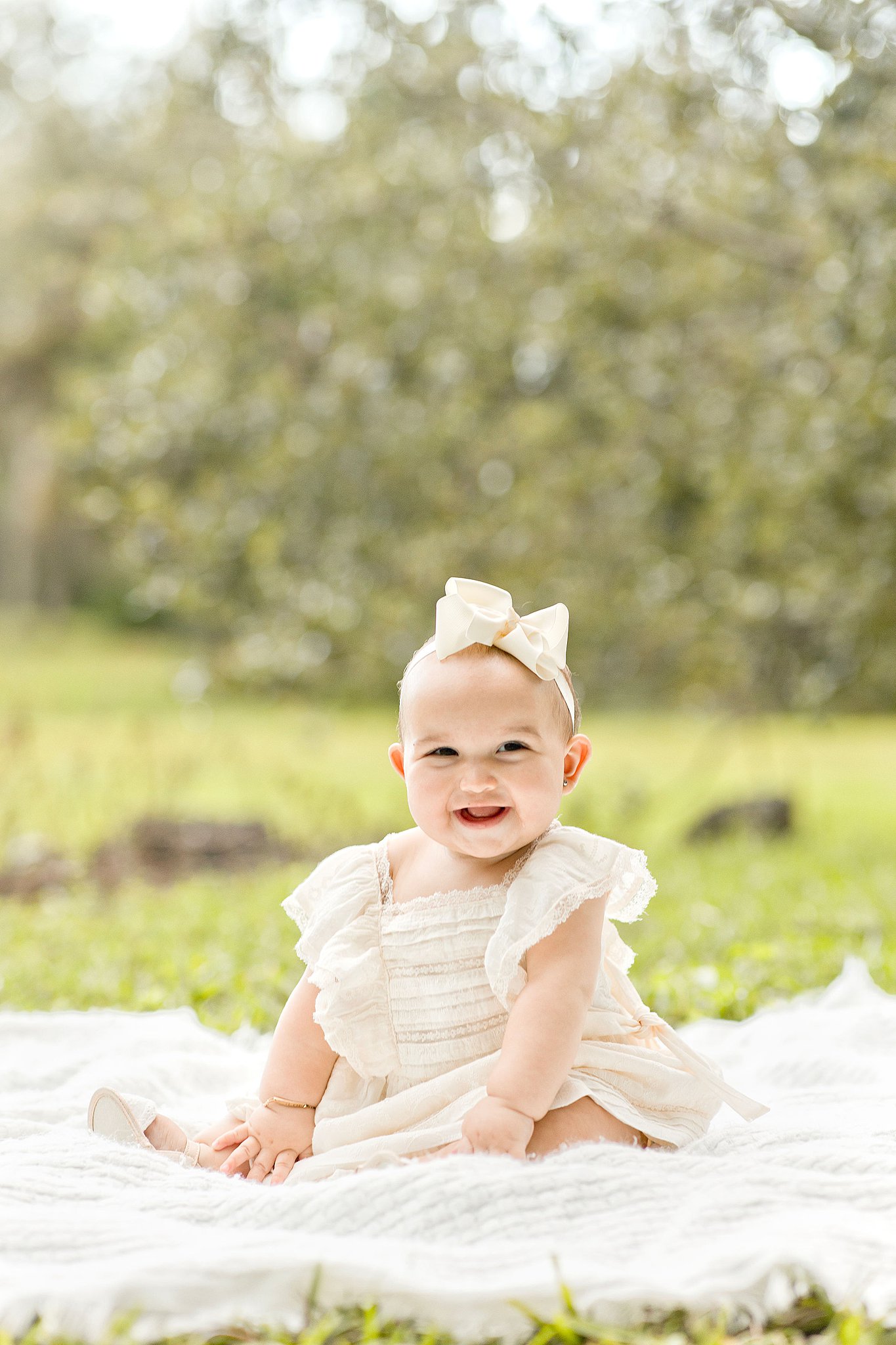 Toddler sits on a blanket in a grassy field wearing a white dress miami beach pediatricians