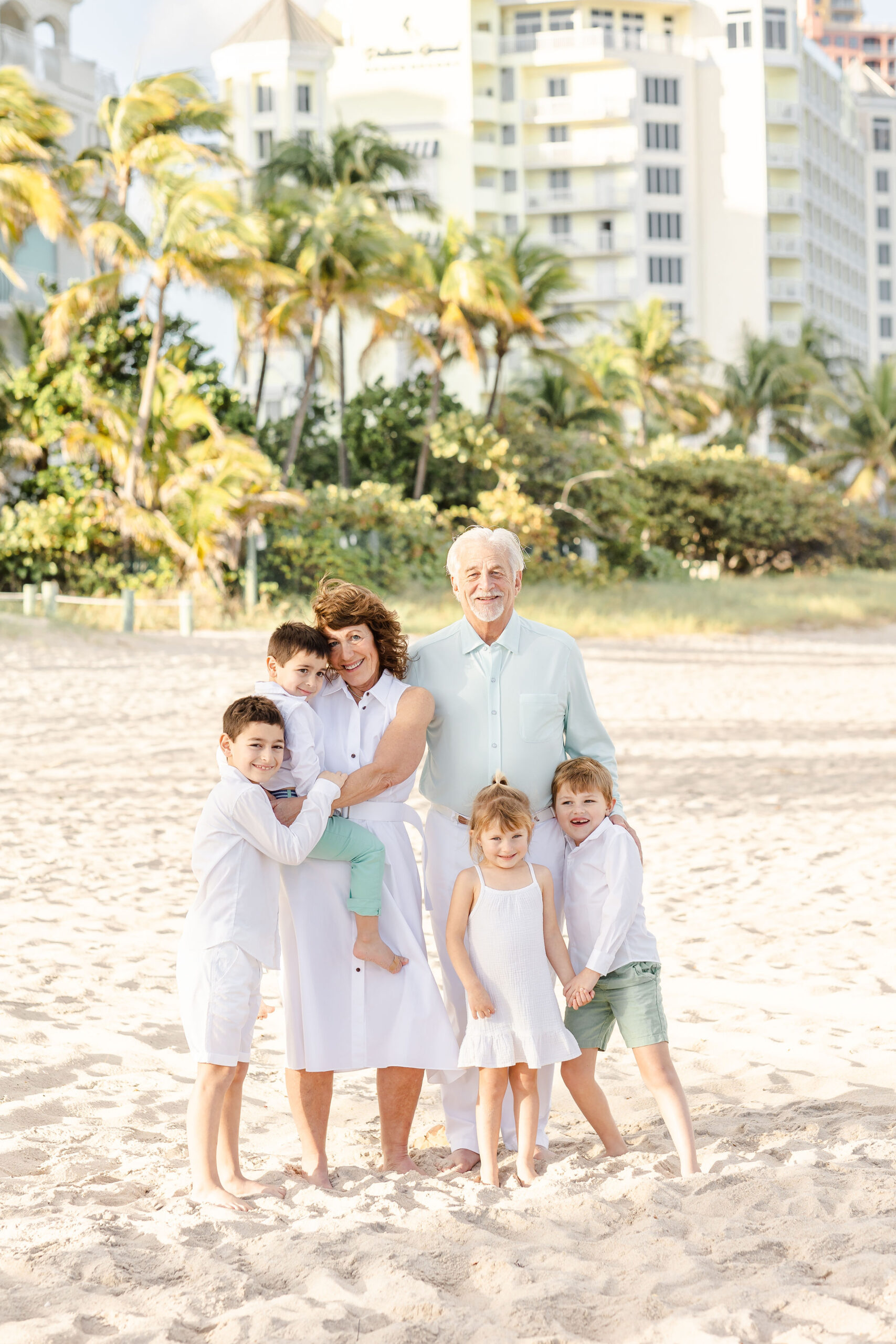 Grandma and grandpa stand on the beach with their four grandchildren