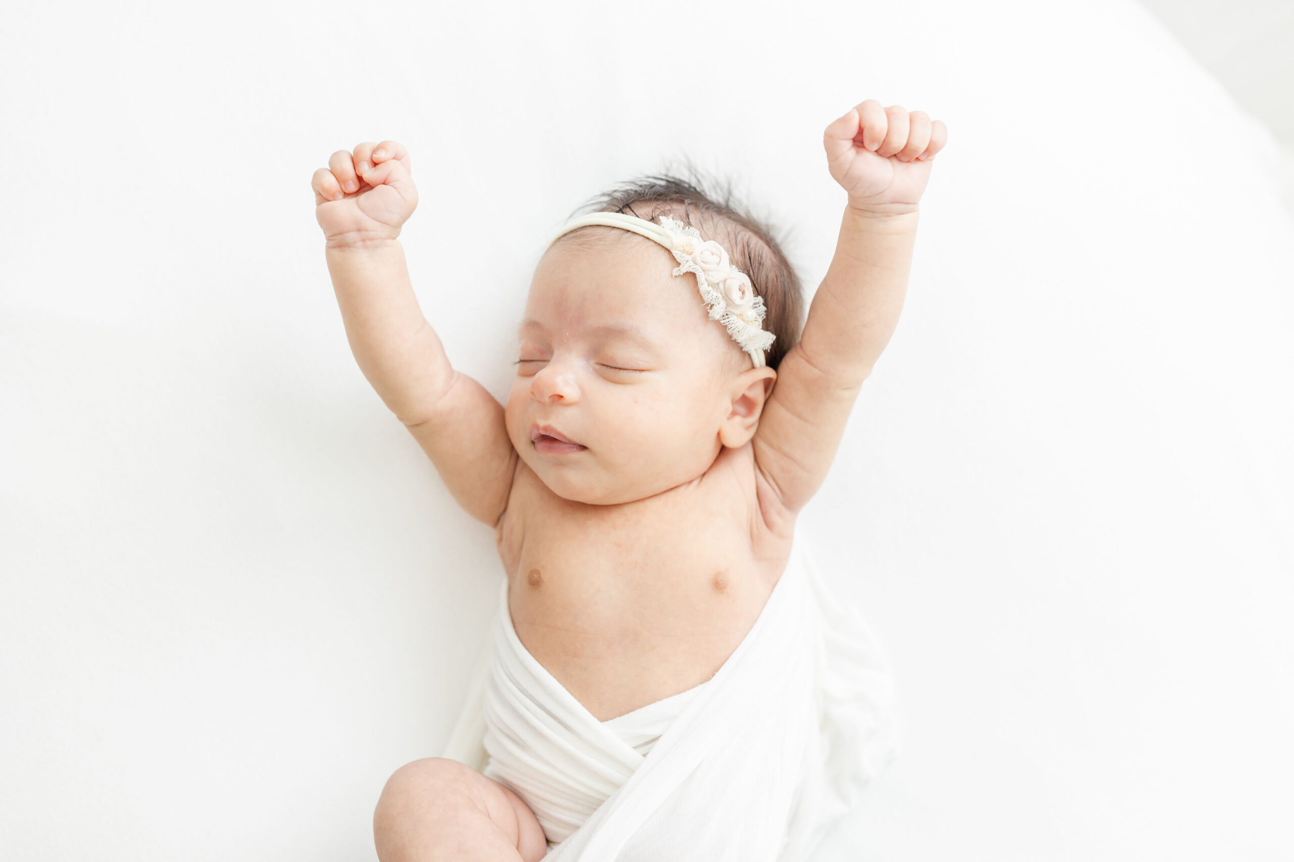 A newborn baby stretches out its arms while sleeping in a white swaddle natural birth choices