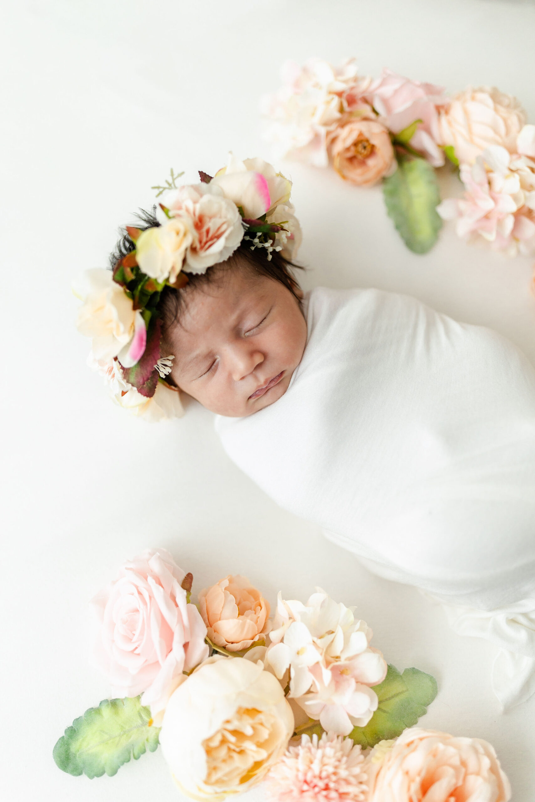 A newborn baby sleeps in a white swaddle surrounded by colorful flowers yoyo boutique