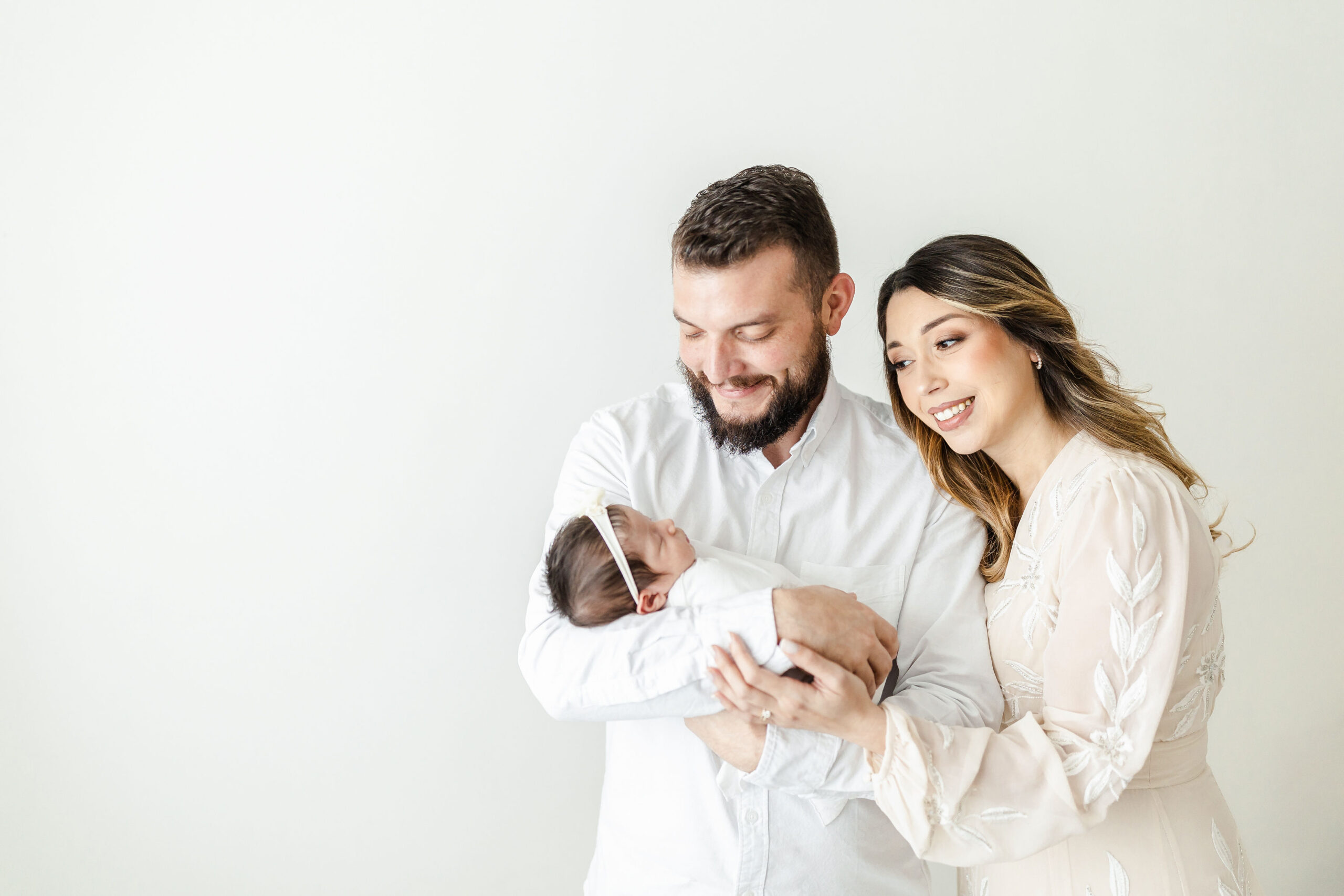 A father and mother looks down at their newborn baby in dad's arms while standing in a studio yoyo boutique