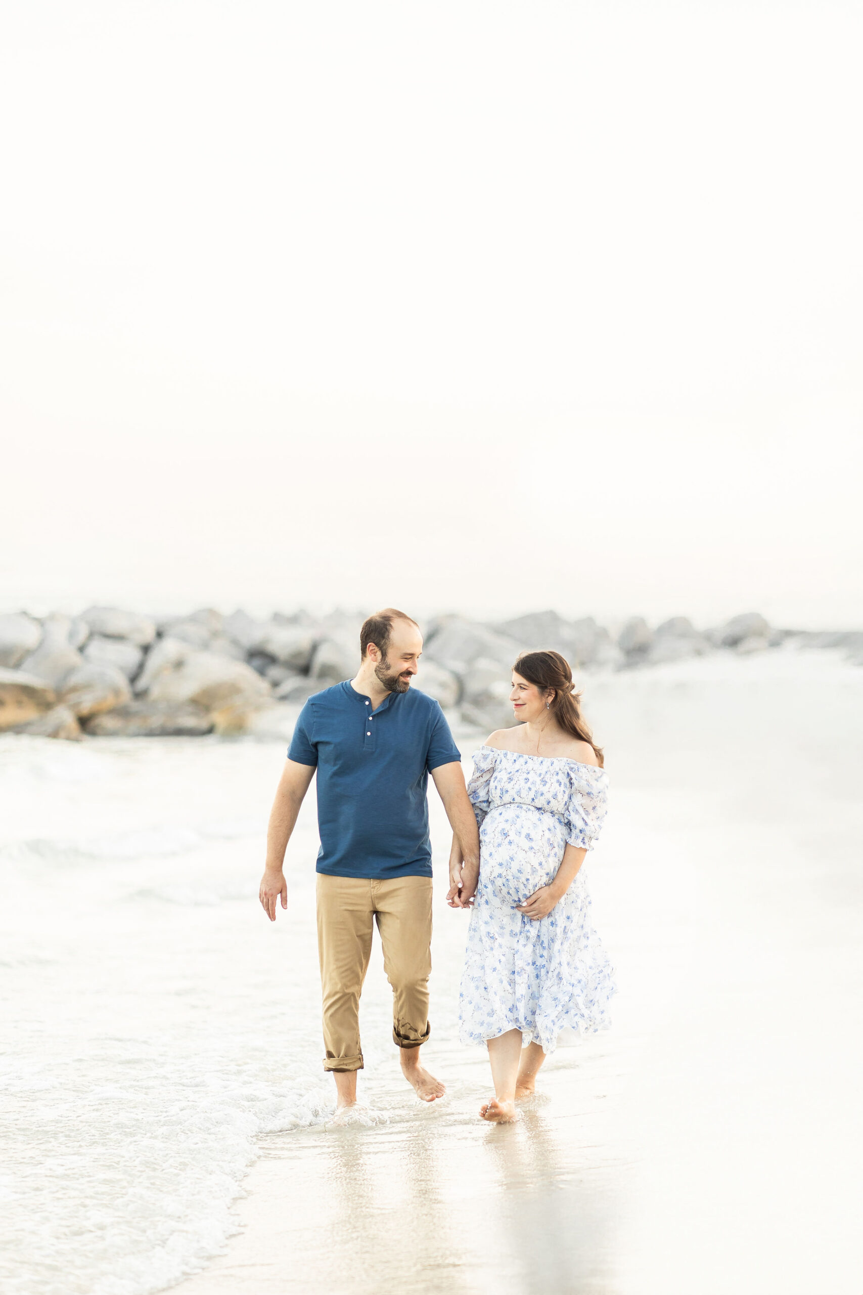 A mom to be and her partner walk down a beach holding hands by in the water fertility acupunture miami