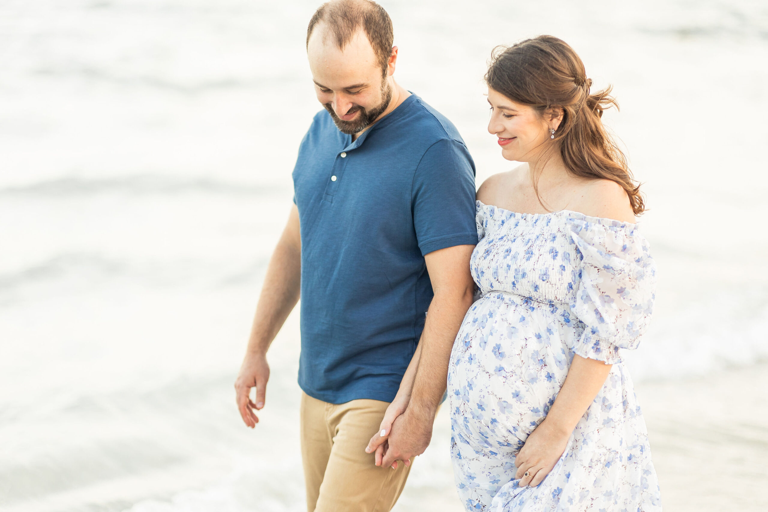 Expecting parents walk down a beach holding hands and smiling fertility acupunture miami