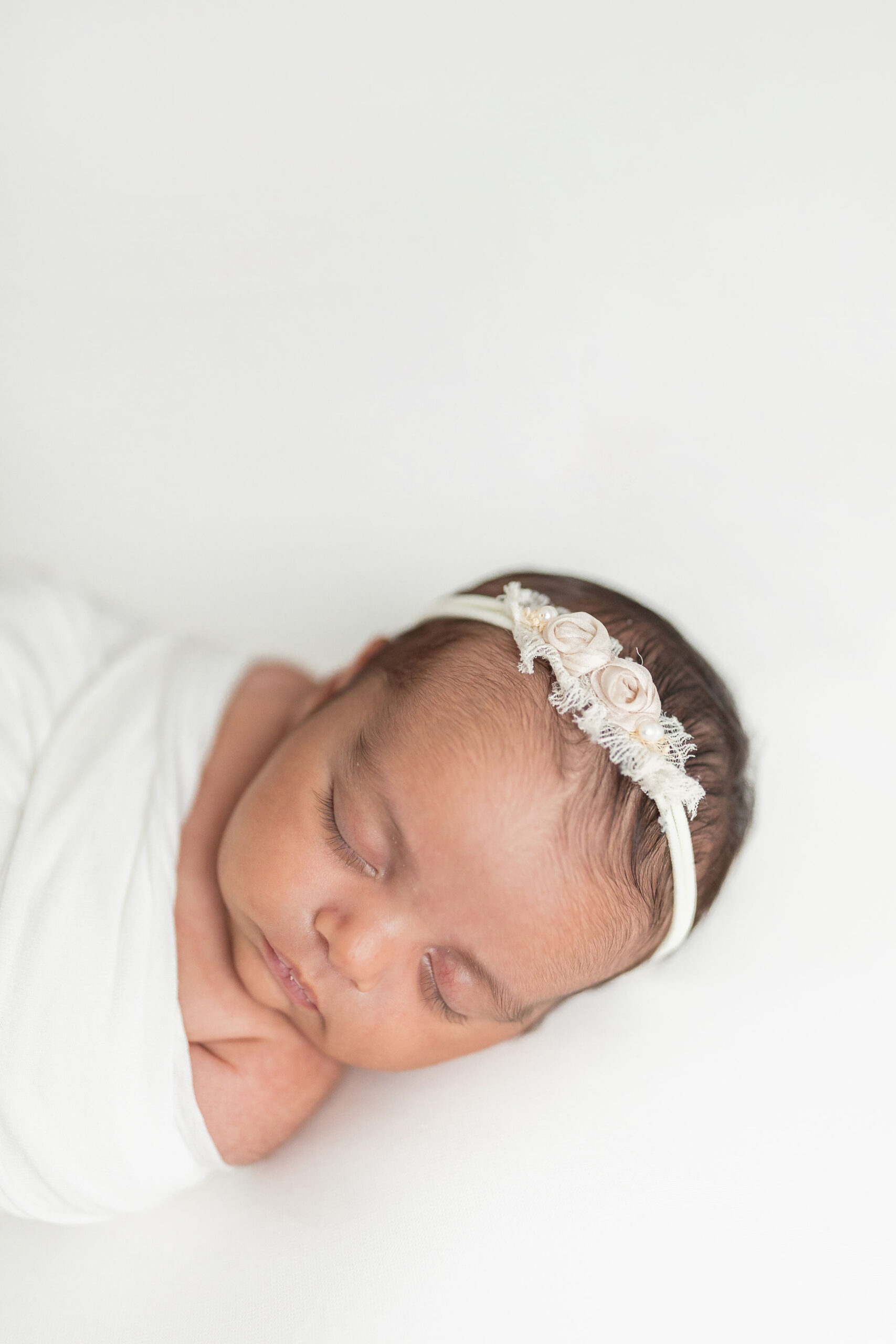 A newborn baby sleeps while wrapped in a swaddle wearing a fabric flower headband namely newborns