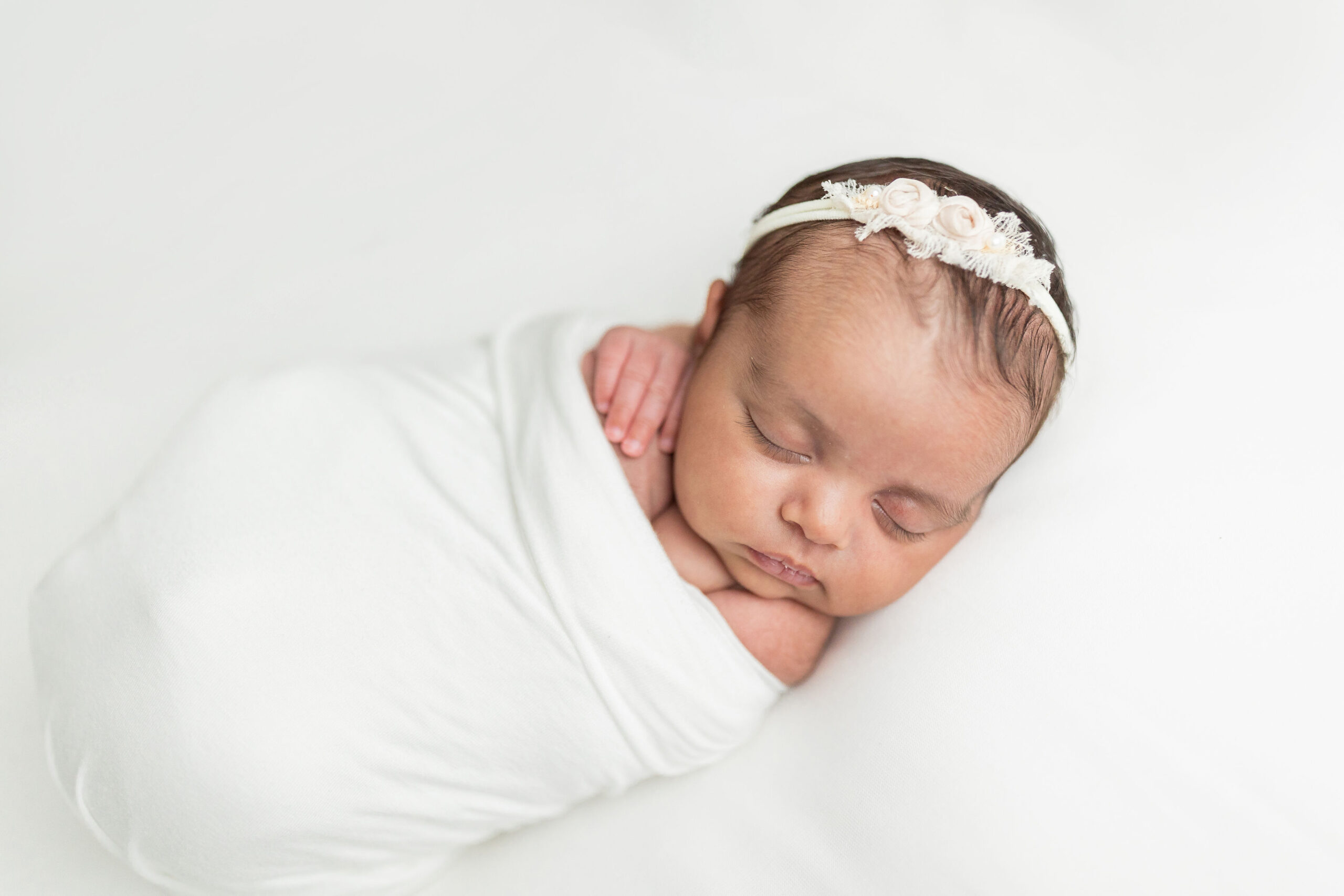 A newborn baby girl sleeps on a white bed in a swaddle in a studio namely newborns