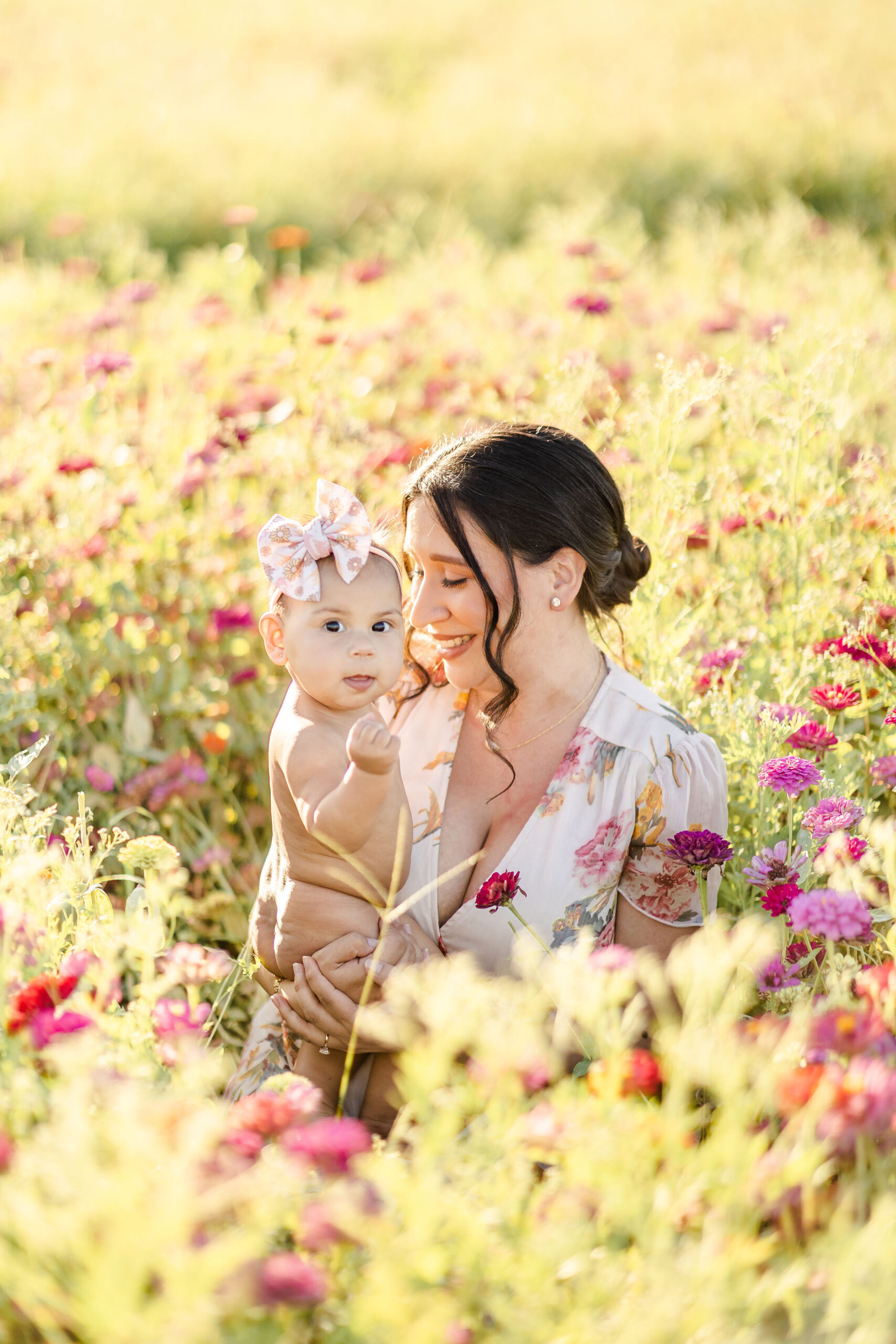 A new mom sits in a field of wildflowers smiling at her infant daughter sitting in her hands with the help of dr gena chiropractic