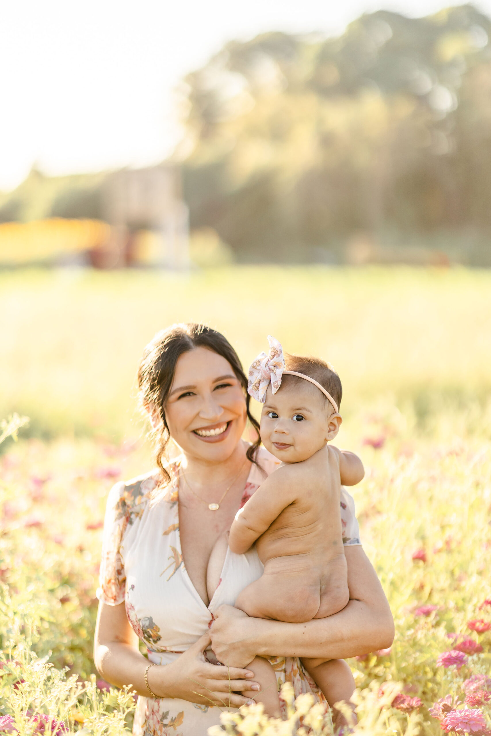 A mother stands in a field of wildflowers holding her naked infant baby on her hip with help from dr gena chiropractic
