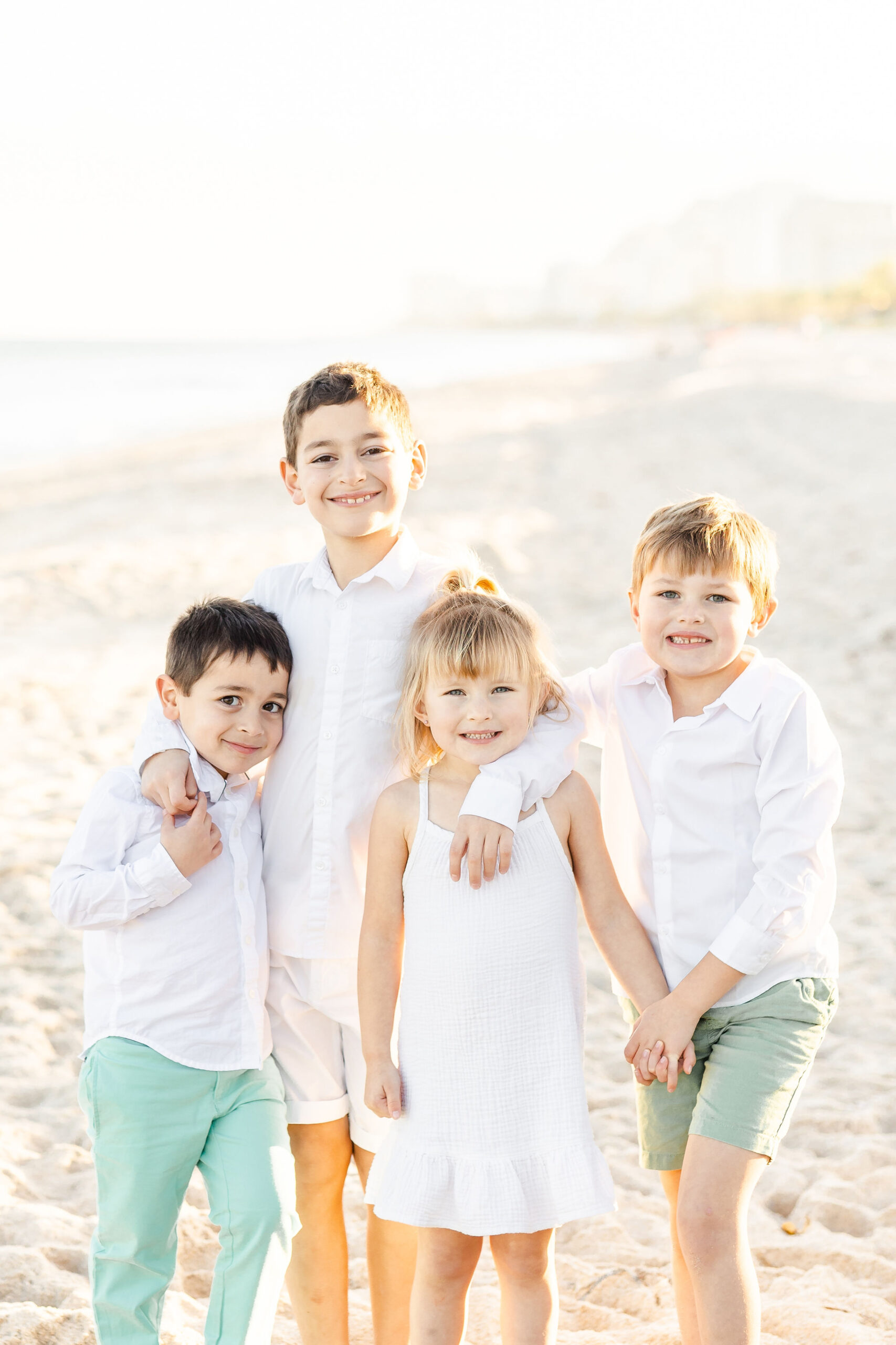 Four siblings stand and lean on each other while holding hands on a beach