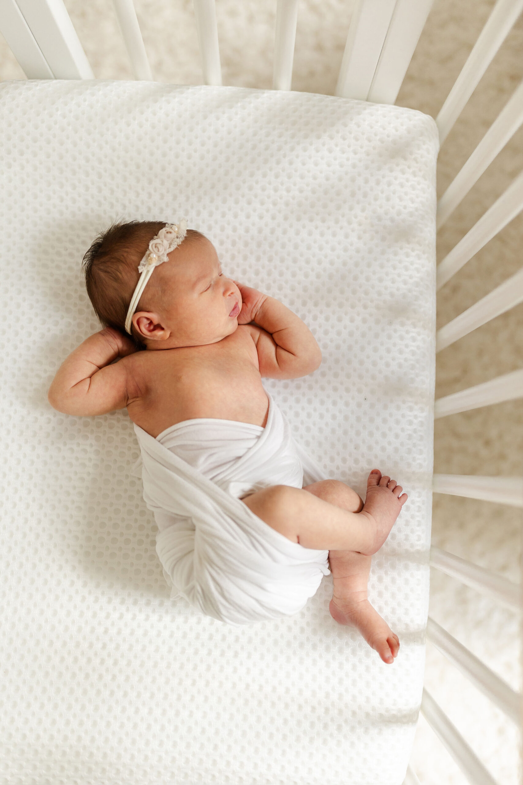 A newborn baby sleeps in a white wrap in a white crib
