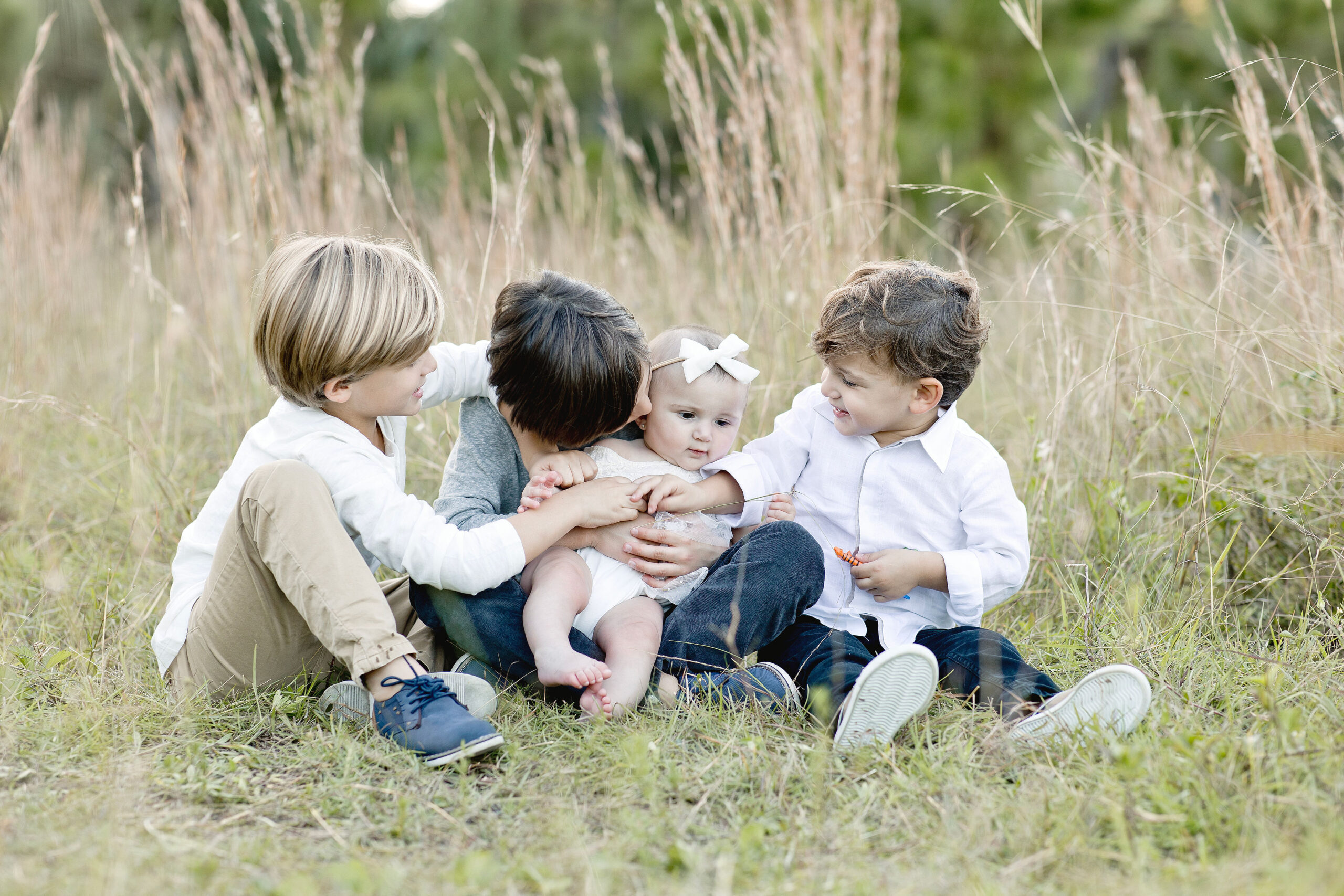 Four siblings play together while sitting in a field of tall grass after attending miami preschools