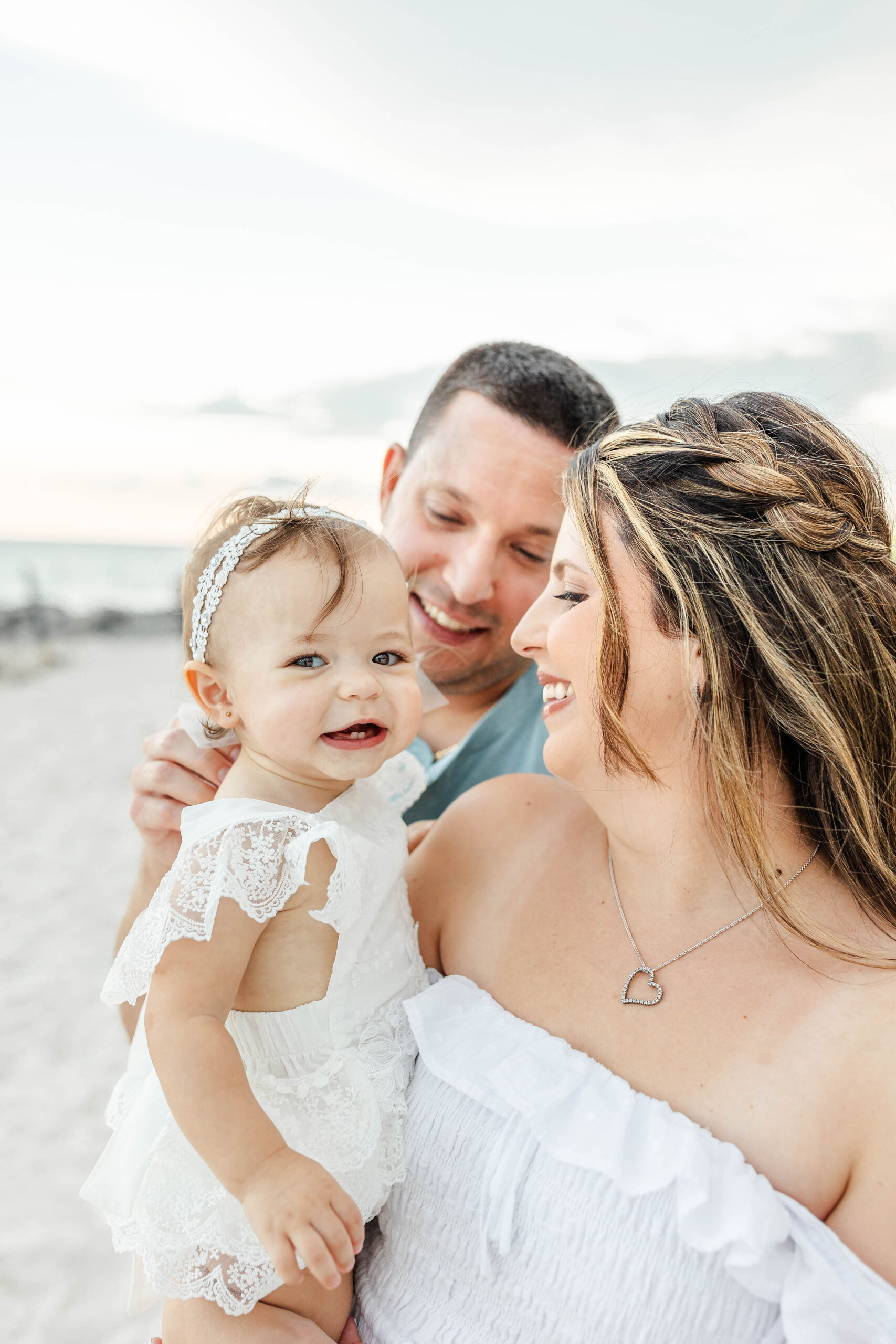 A mother and father walk down a beach laughing with their toddler daughter in mom's arms during things to do in miami with toddlers