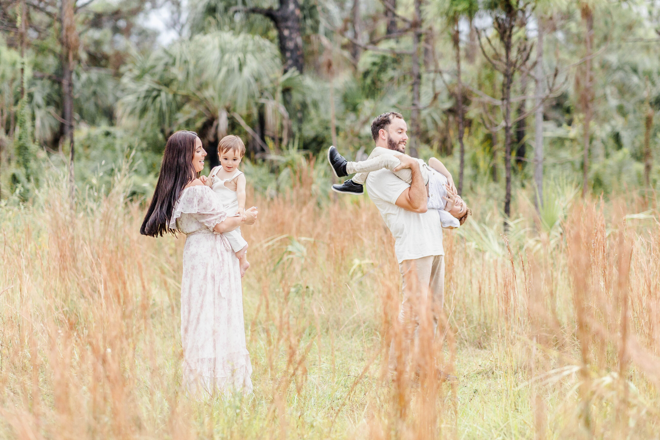 A happy family plays and laughs while exploring a field of tall grass in white