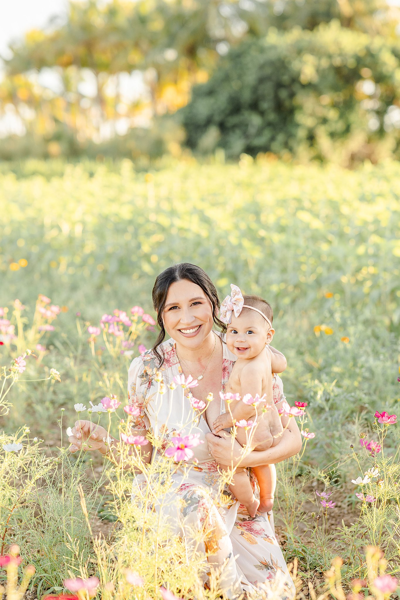 A happy mom explores a field of wildflowers with her smiling infant daughter in her arms