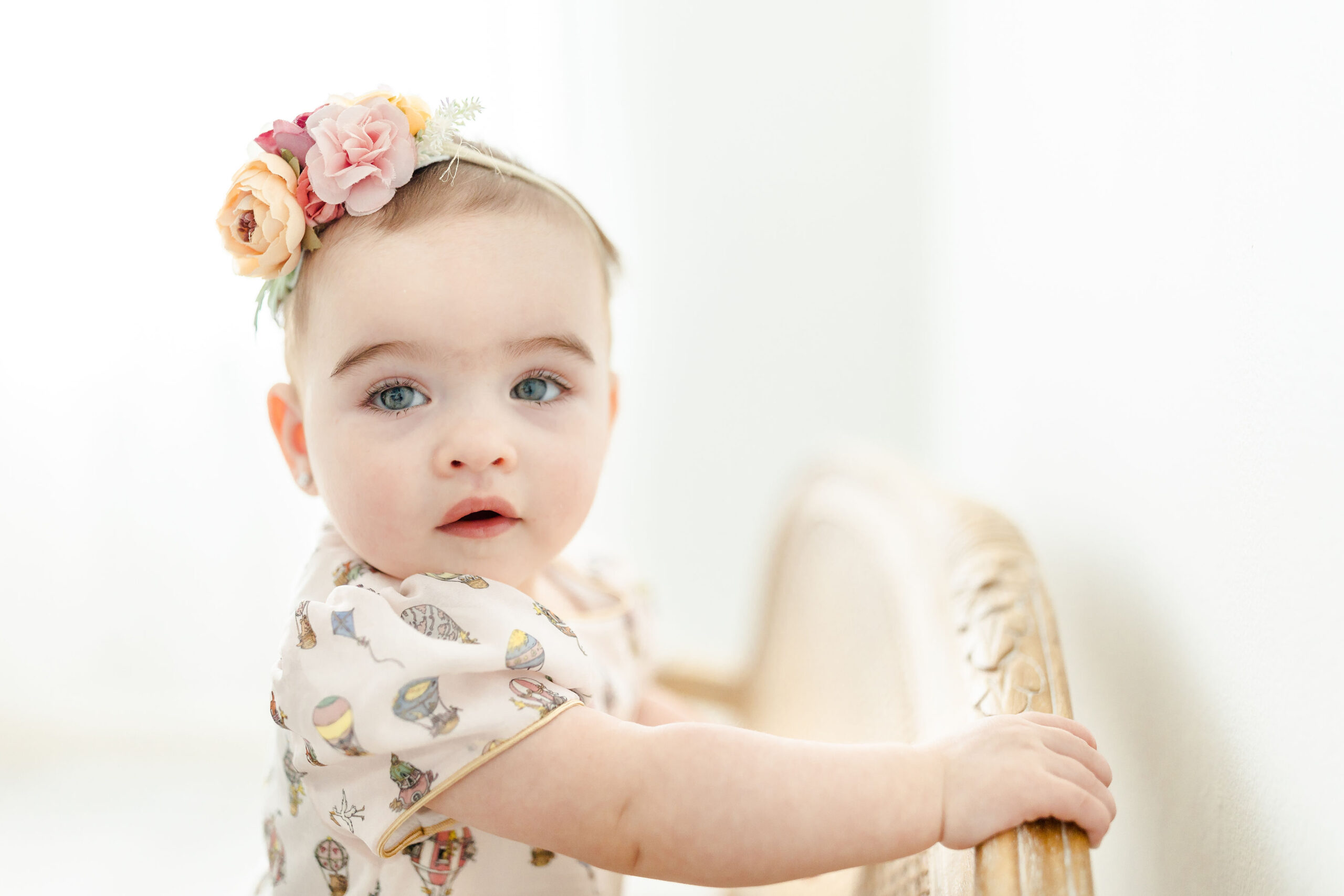 A toddler girl climbs on a bench in a print onesie and floral headband in a studio before visiting indoor playgrounds in miami