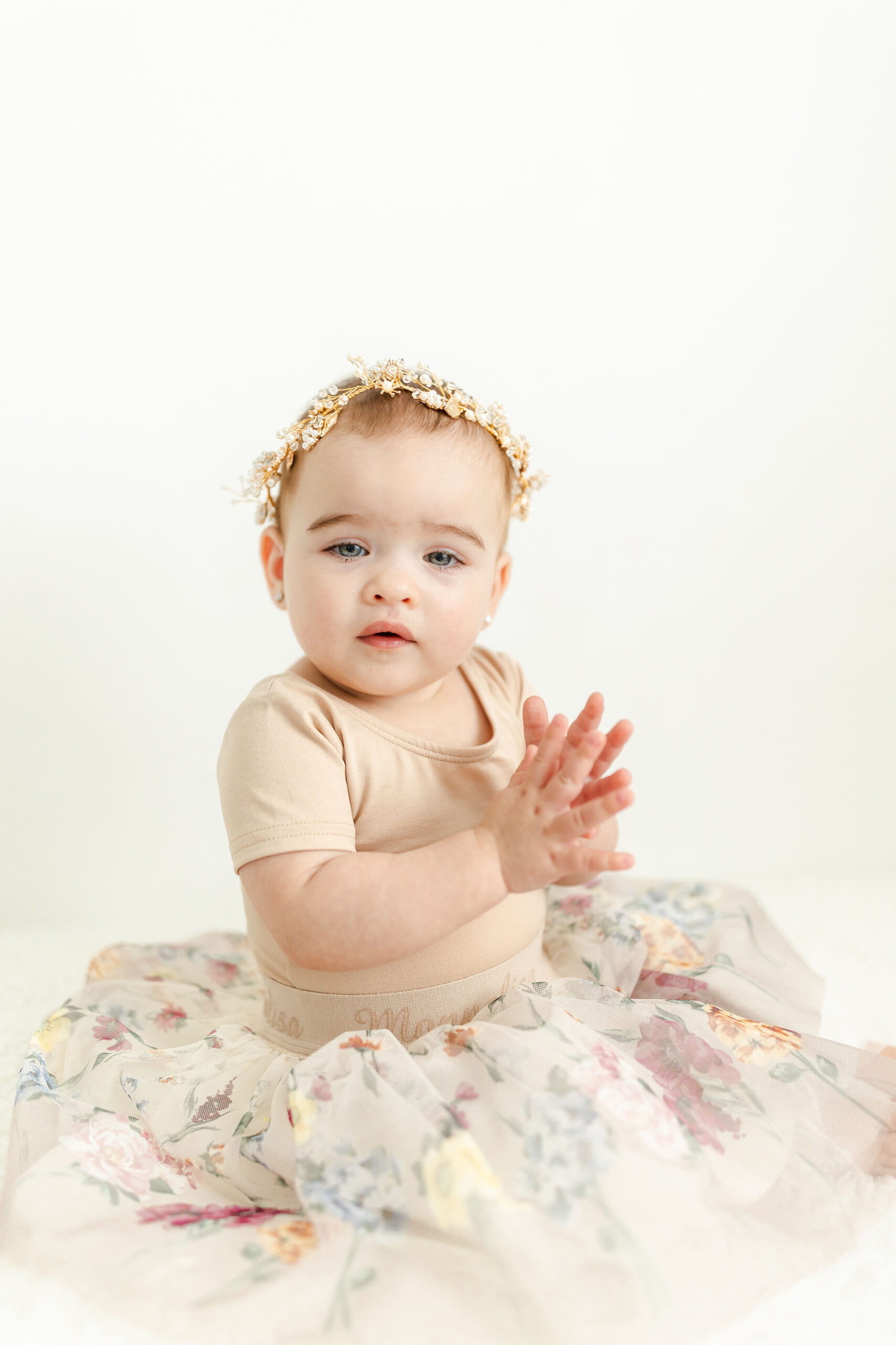 A toddler girl in a floral dress claps while sitting on the floor of a studio before visiting indoor playgrounds in miami