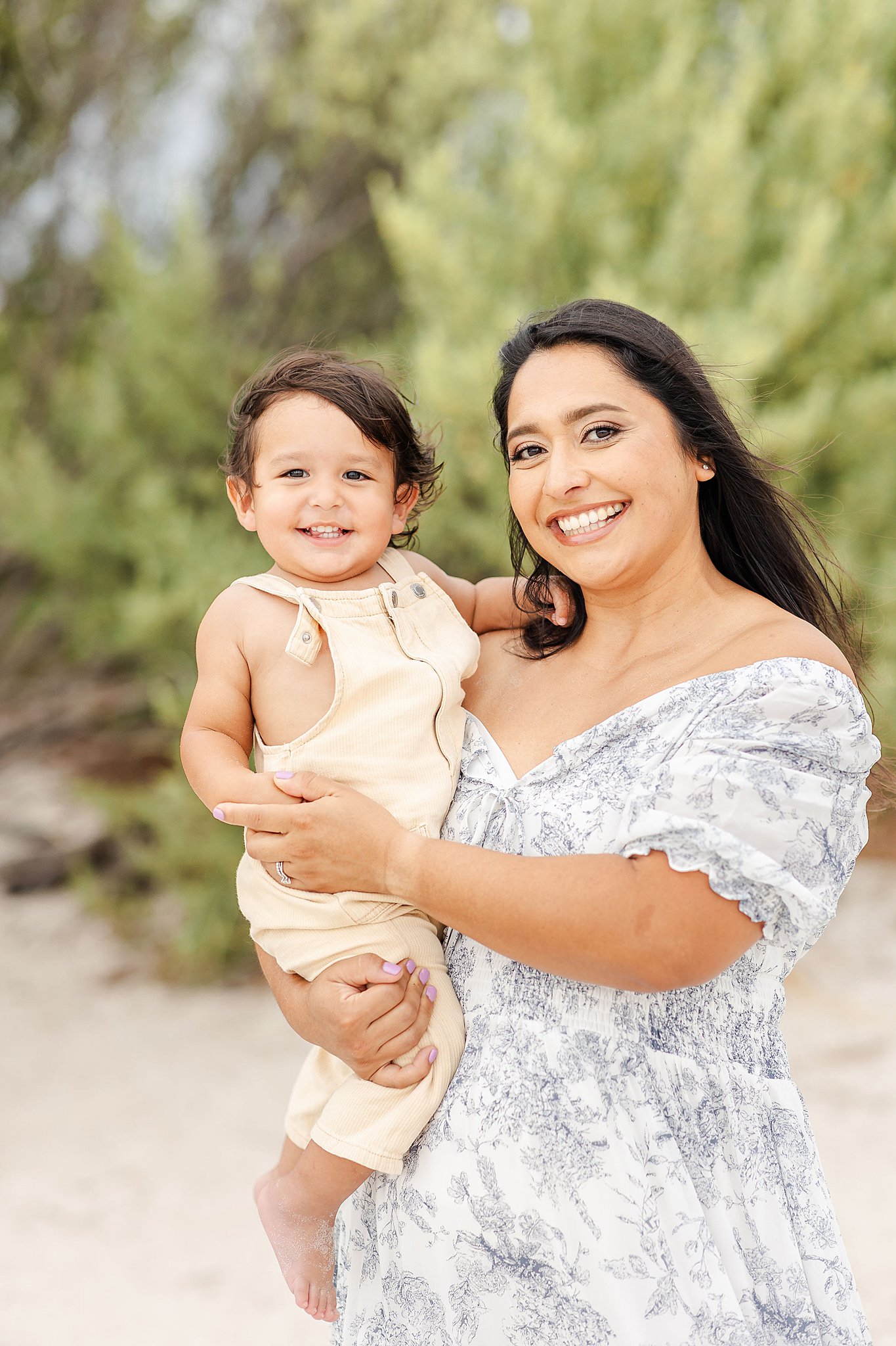 A happy toddler sits in mom's arms while exploring a windy beach before visiting kid friendly restaurants miami