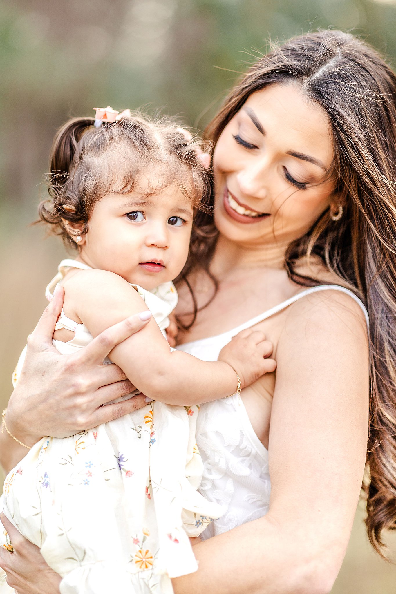 A toddler girl holds onto mom while sitting in her arms before visiting pumpkin patches miami