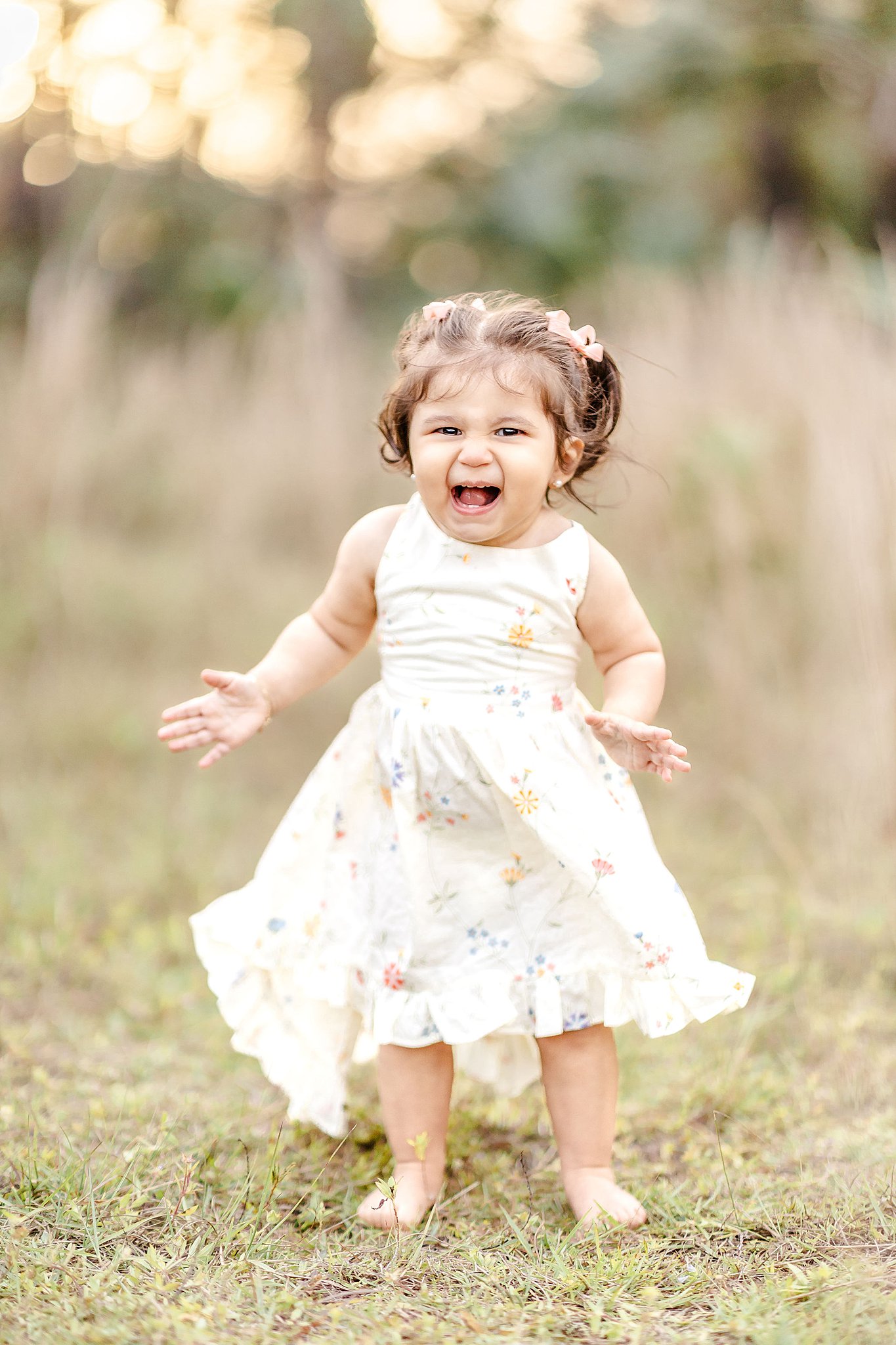 A happy toddler girl giggles while walking in a field at sunset in a white flower dress before visiting pumpkin patches miami