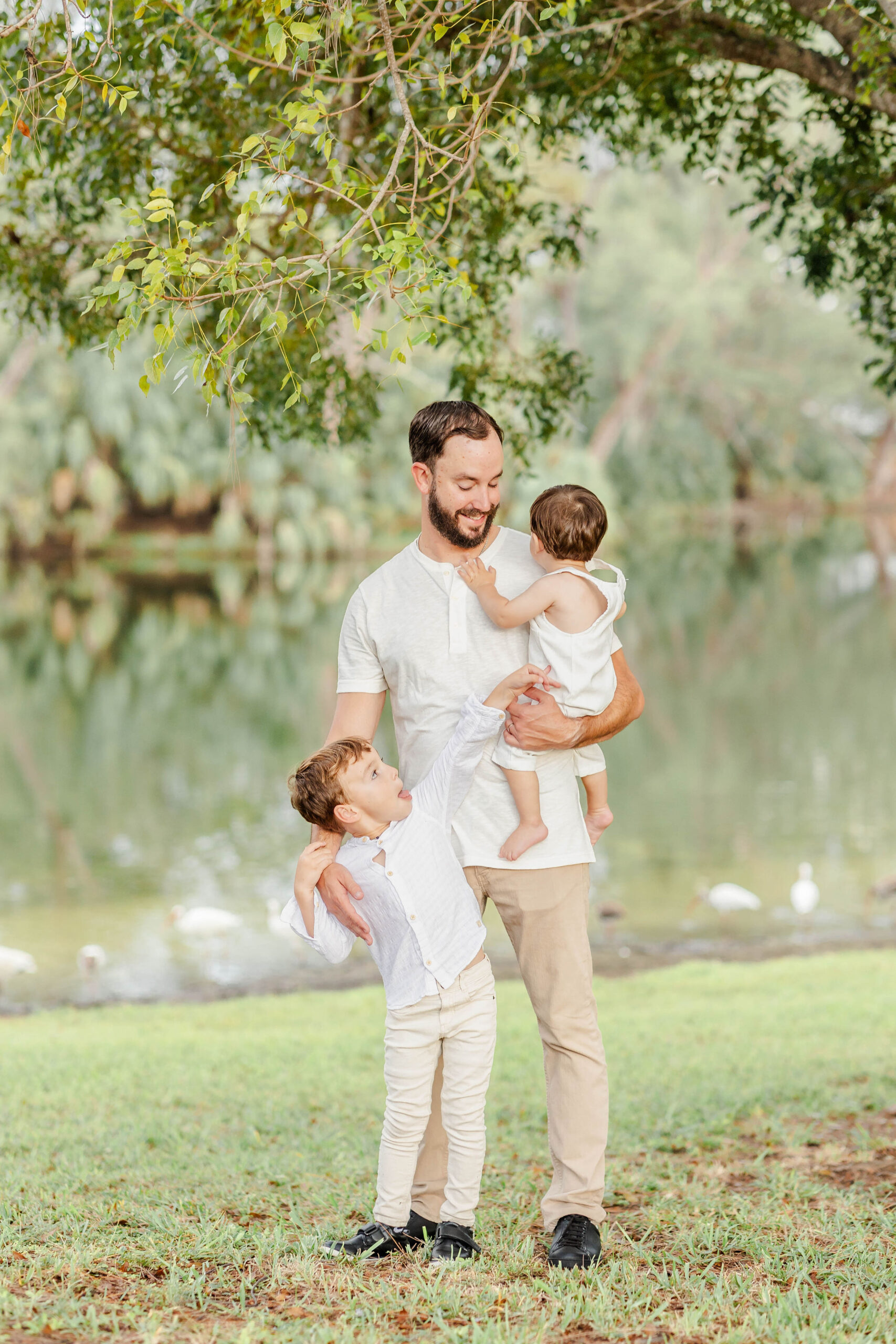 Happy dad stands under an oak tree playing with his toddler sons before visiting trampoline parks miami